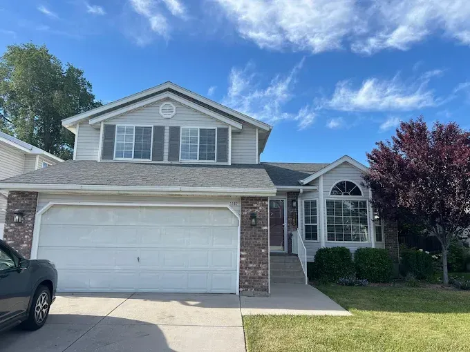 Two-story house with light gray siding, a white garage door, and a small front yard under a blue sky.