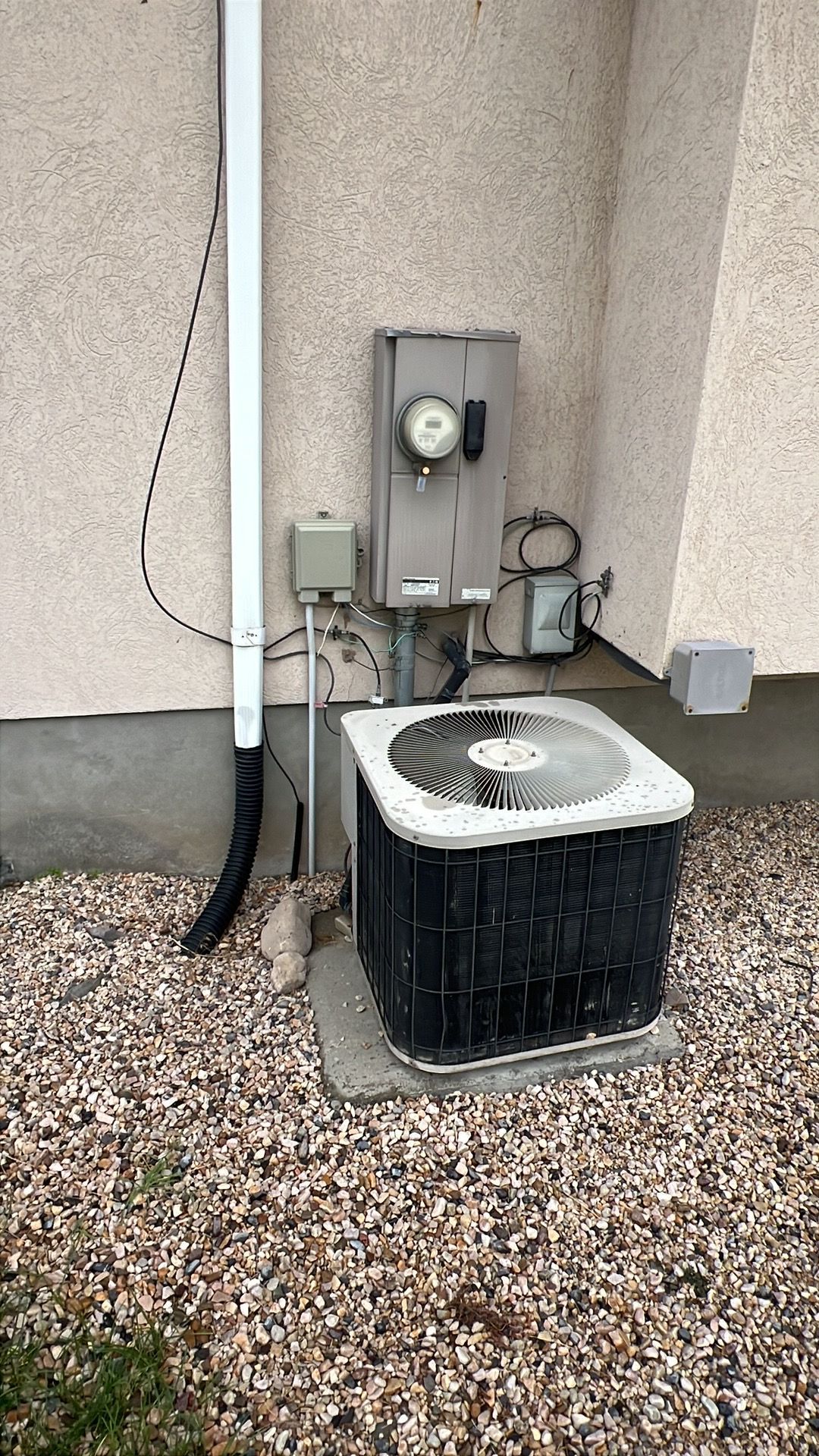 Outdoor air conditioning unit next to electrical box and house siding on a bed of gravel.