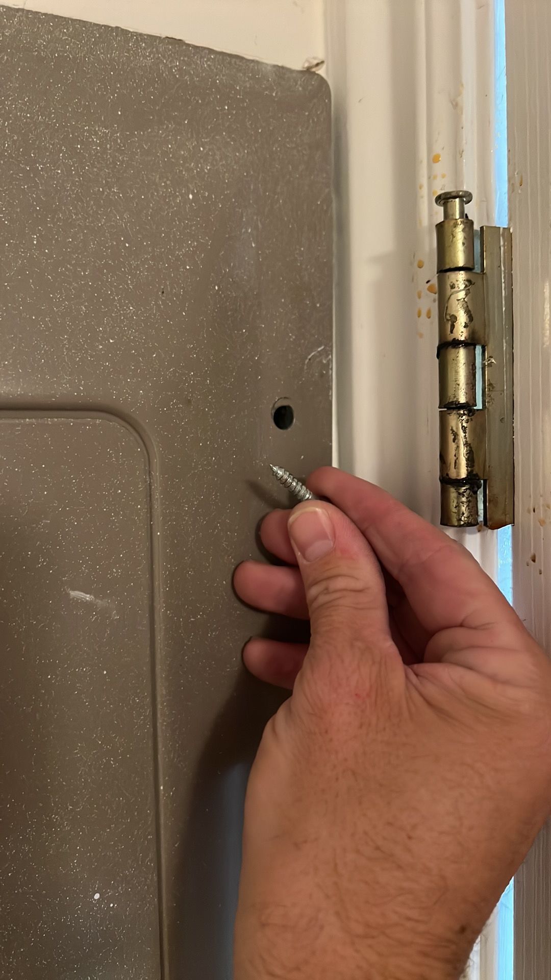 Hand holding a screw near a door and hinge, preparing to attach it.