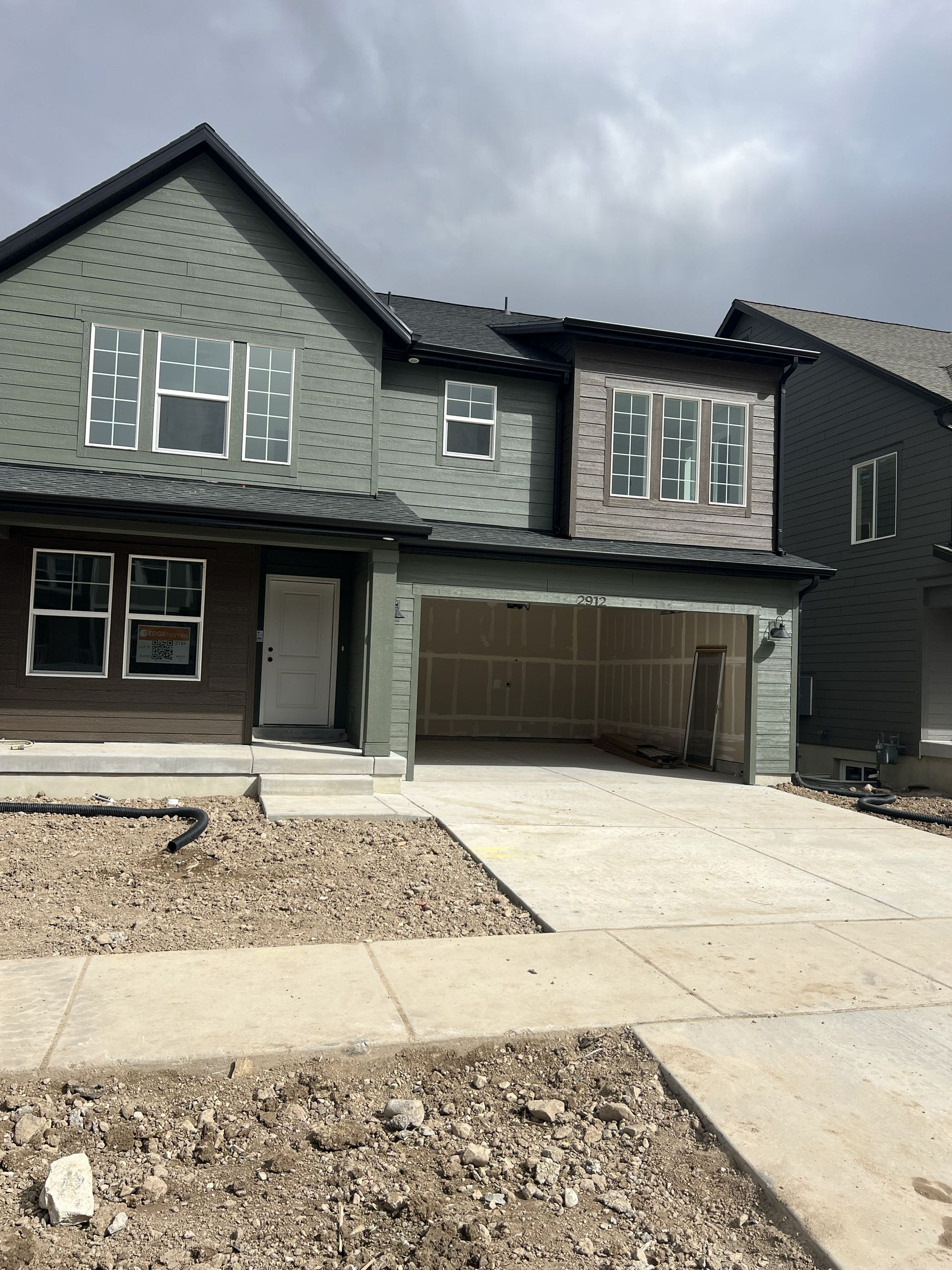 New two-story house under construction with a garage and unfinished landscaping. Green siding, overcast sky.
