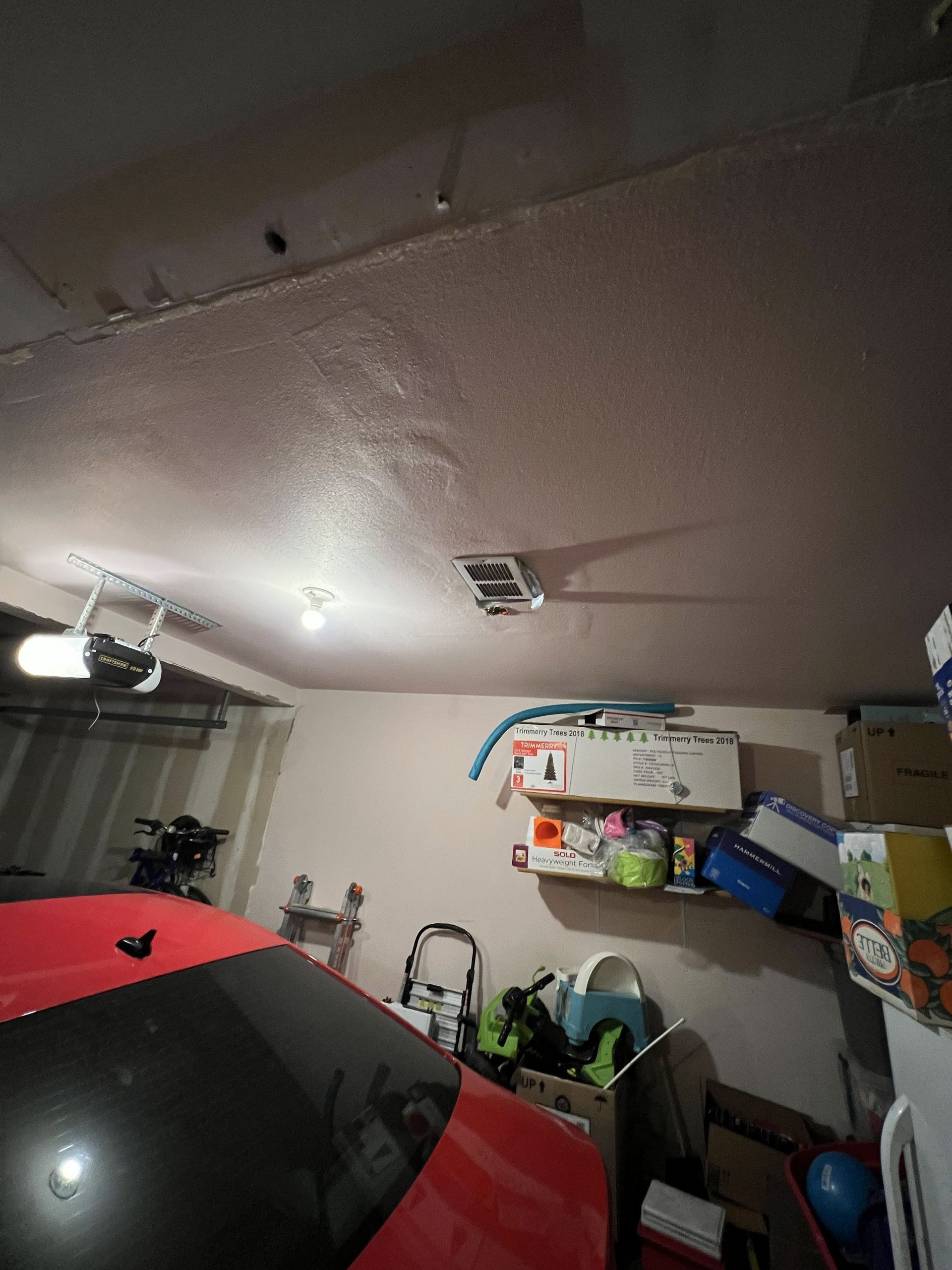 Garage interior with a red car, shelves with boxes, and a textured ceiling.