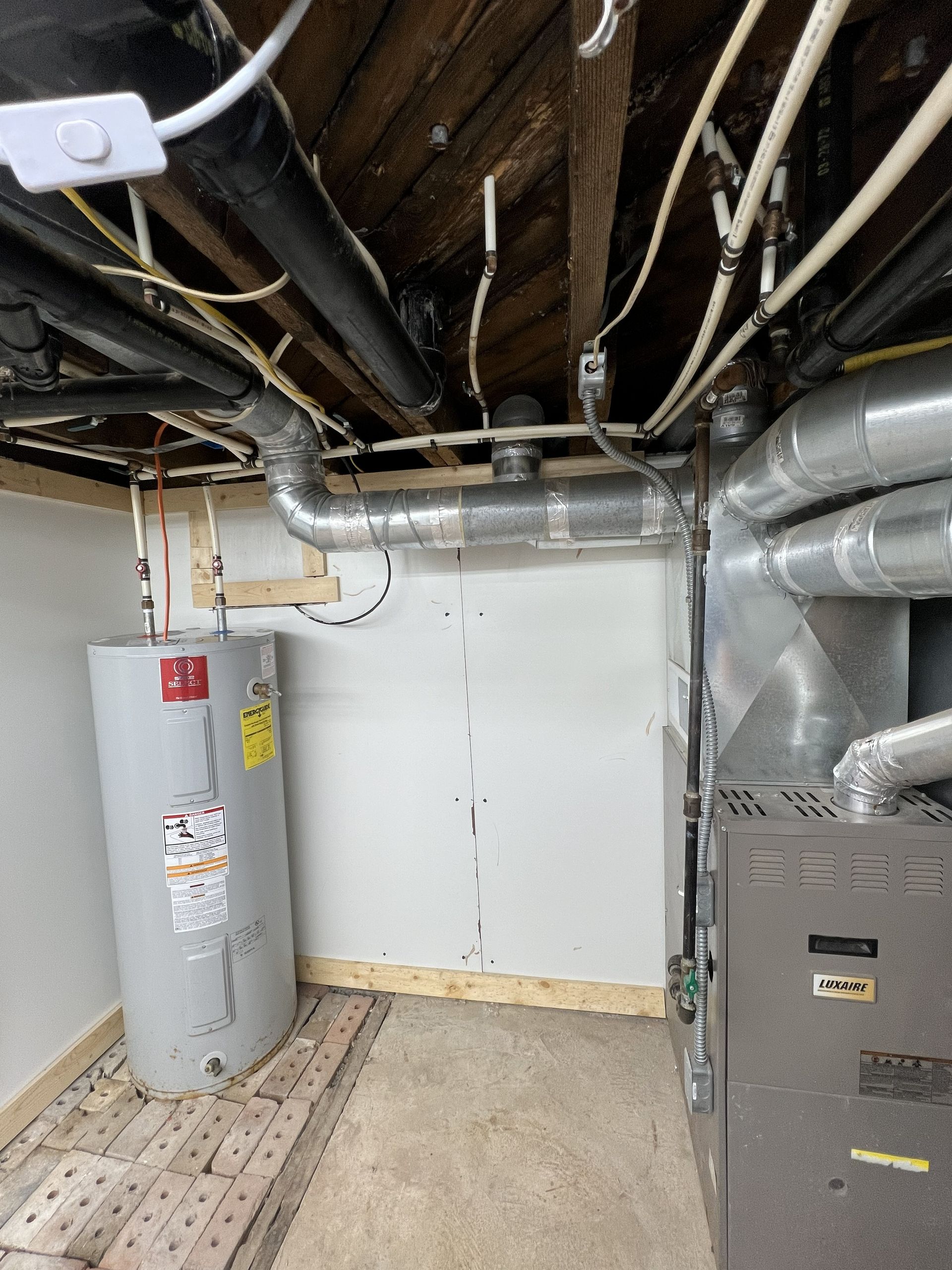 Basement with water heater, furnace, pipes, and ductwork. Grey, white, and wood tones are visible.