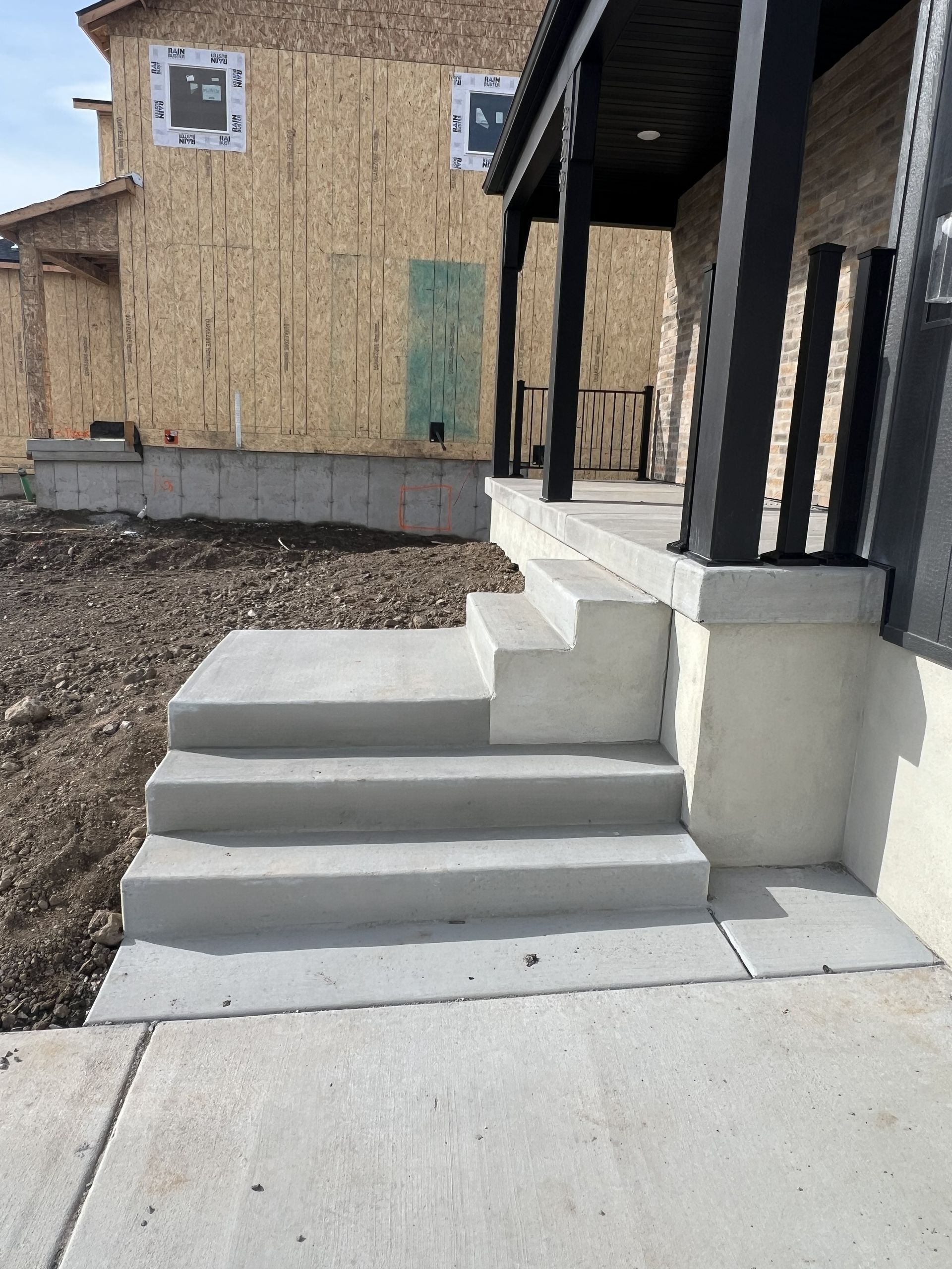 Concrete steps leading up to a porch with black supports; a house under construction in the background.