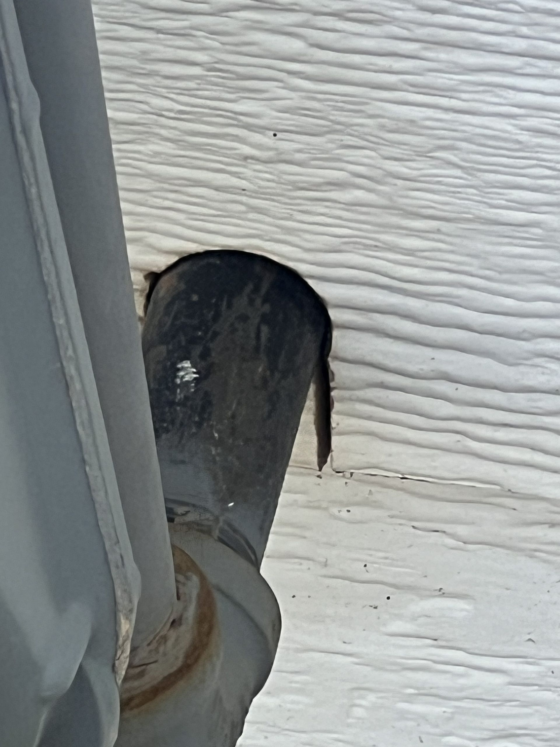 Black exhaust pipe in snow, next to a light-colored structure.