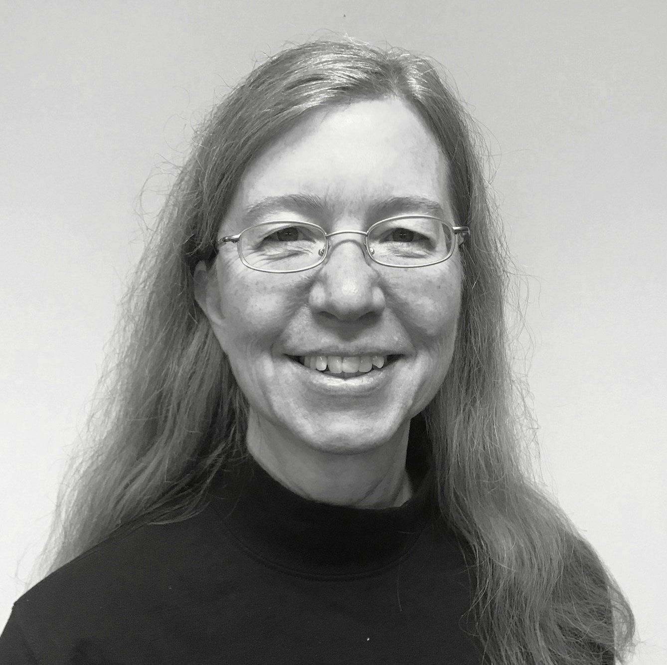 A woman wearing glasses and a black shirt is smiling in a black and white photo.