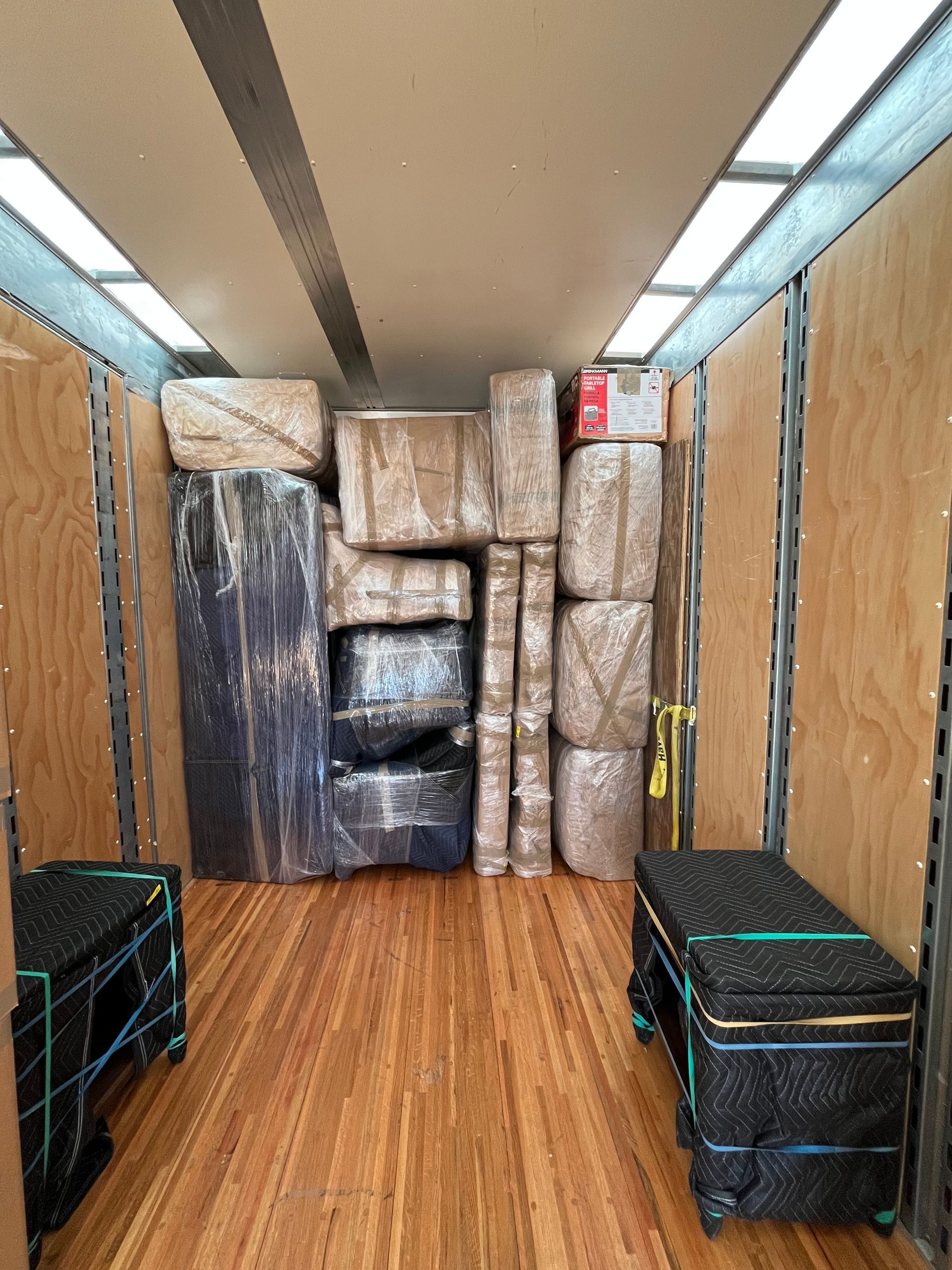 Inside a moving truck, packed with wrapped furniture and boxes. Wooden floor and walls.