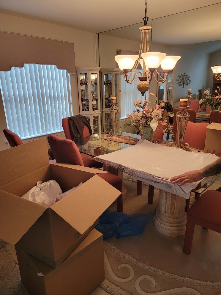 A dining room with a table and chairs and boxes on the floor.