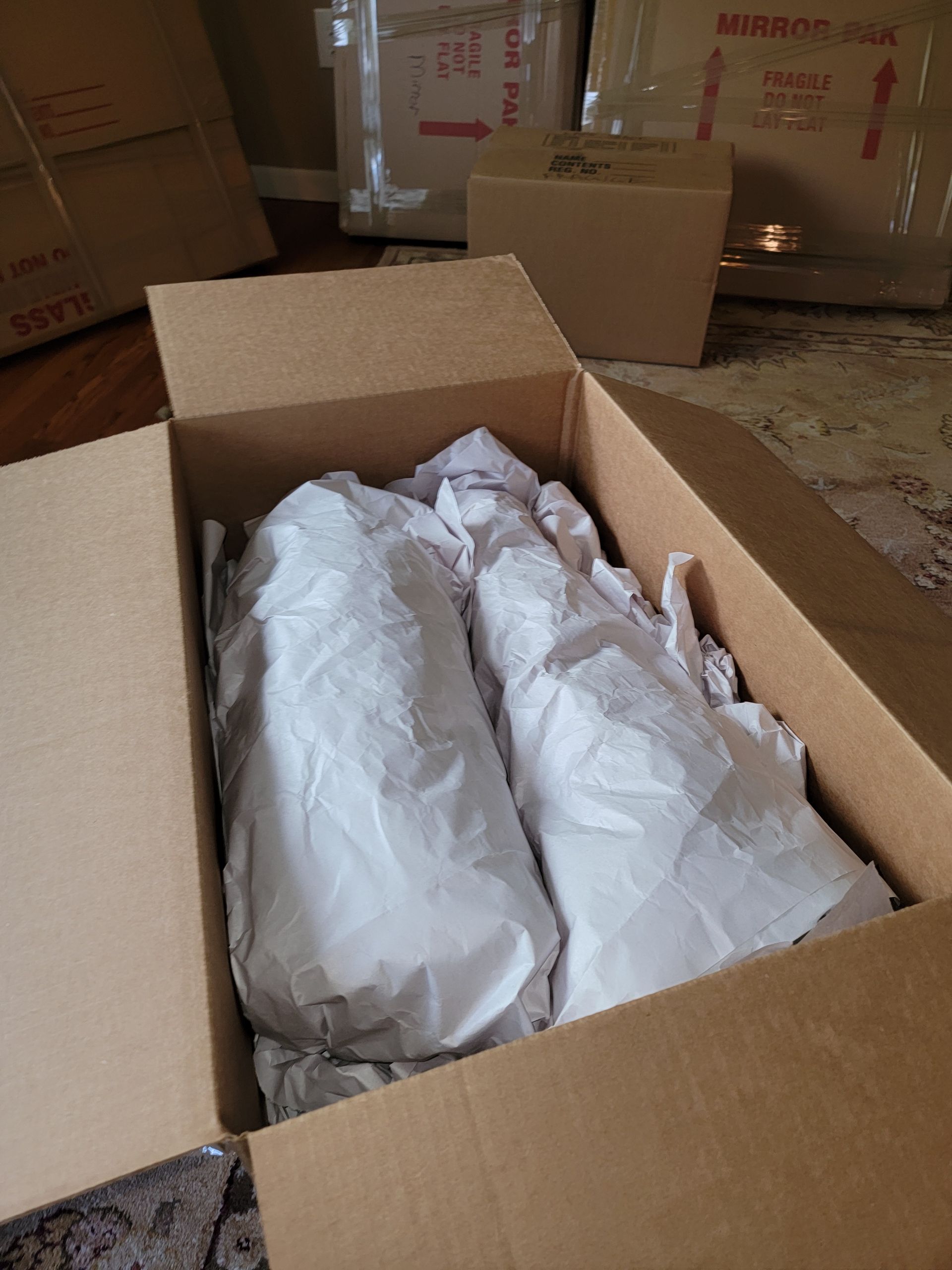 Cardboard box containing two objects wrapped in white paper.
