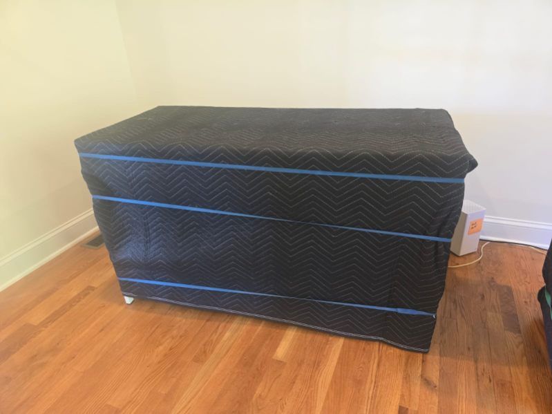 A black blanket is covering a dresser on a wooden floor.