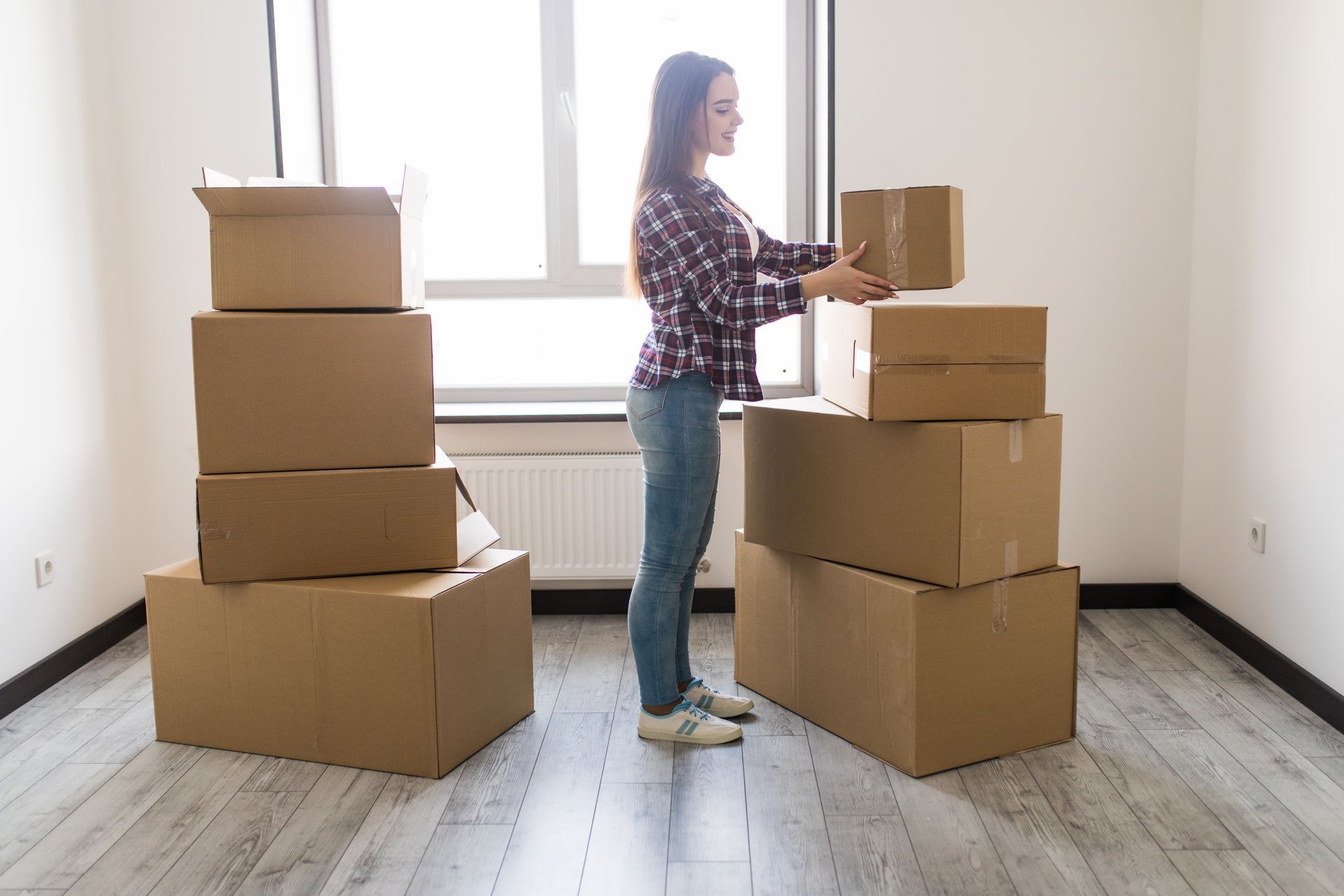 Woman stacking cardboard boxes in a brightly lit room, preparing to move.
