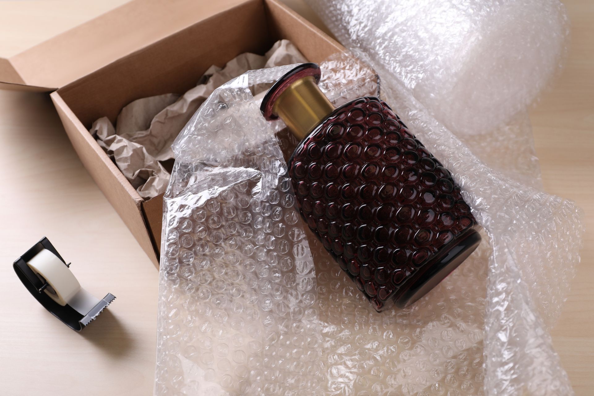 A decorative glass bottle wrapped in bubble wrap, next to a cardboard box and tape dispenser.
