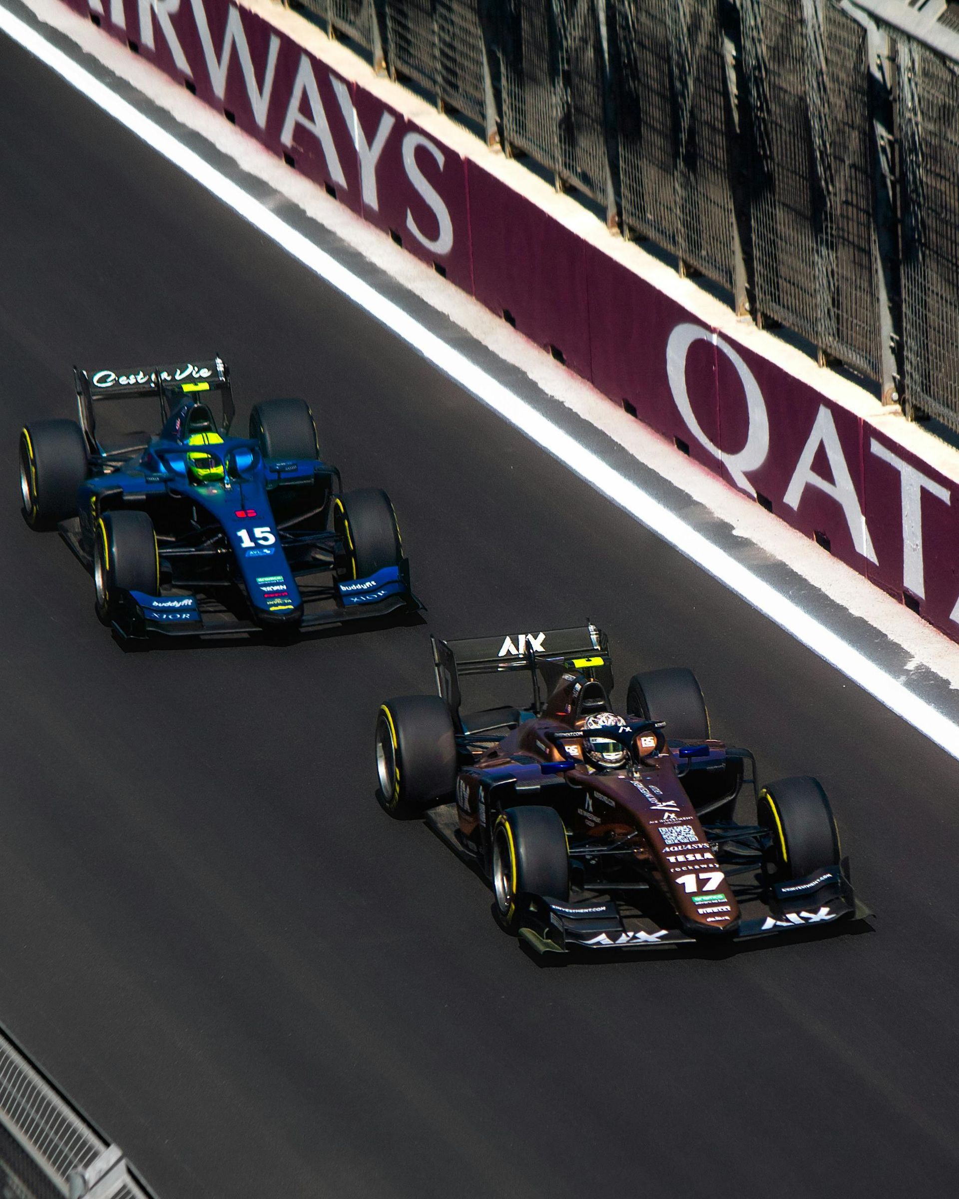 Two race cars on a track with qatar written on the side