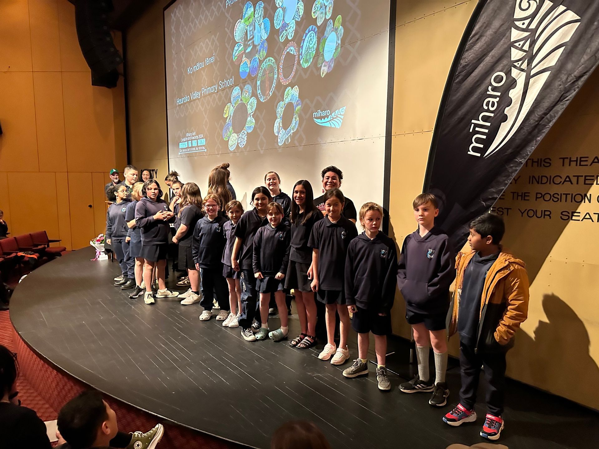 A group of children are standing on a stage in front of a large screen.
