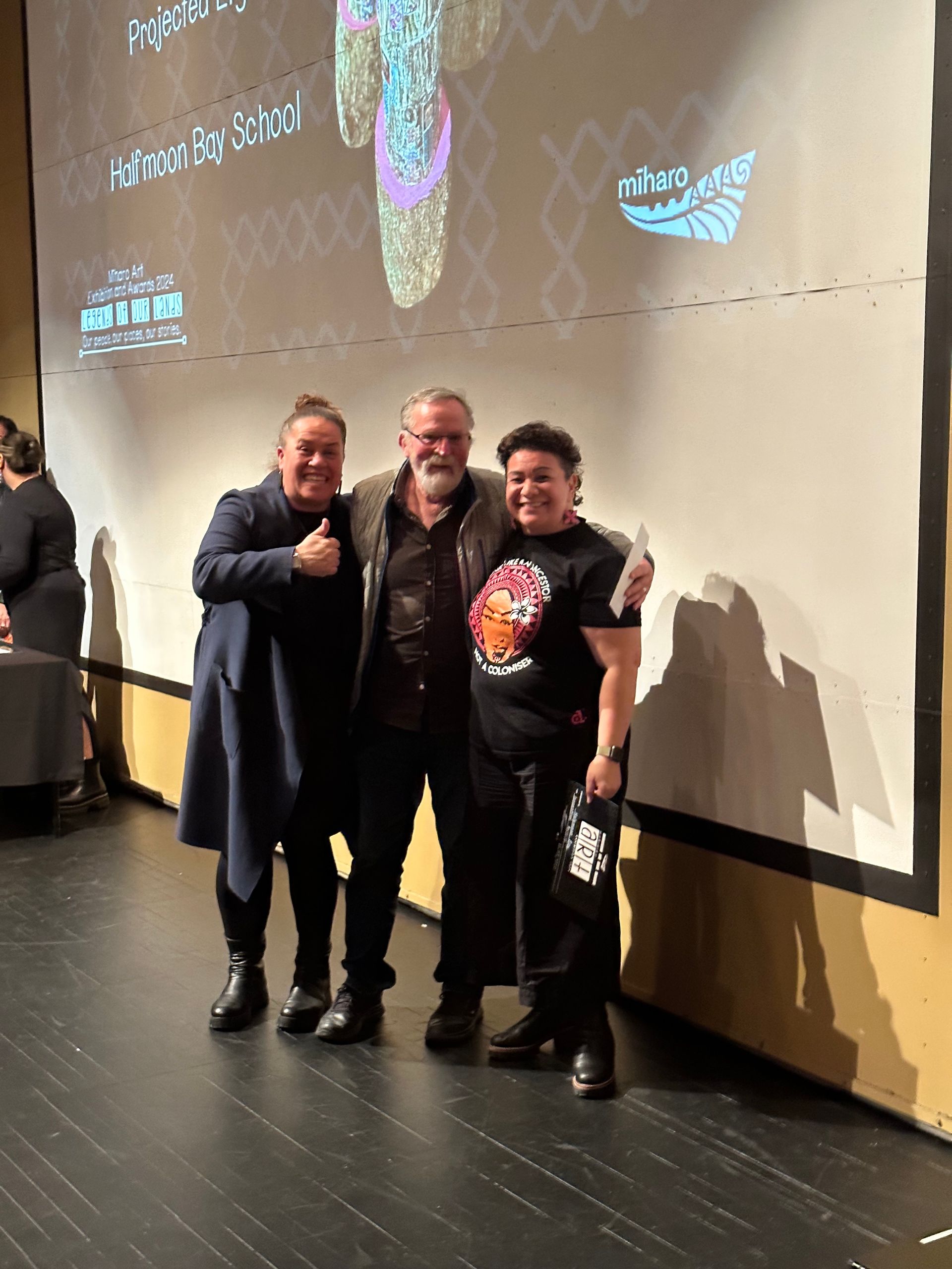 Three men are posing for a picture in front of a large screen.