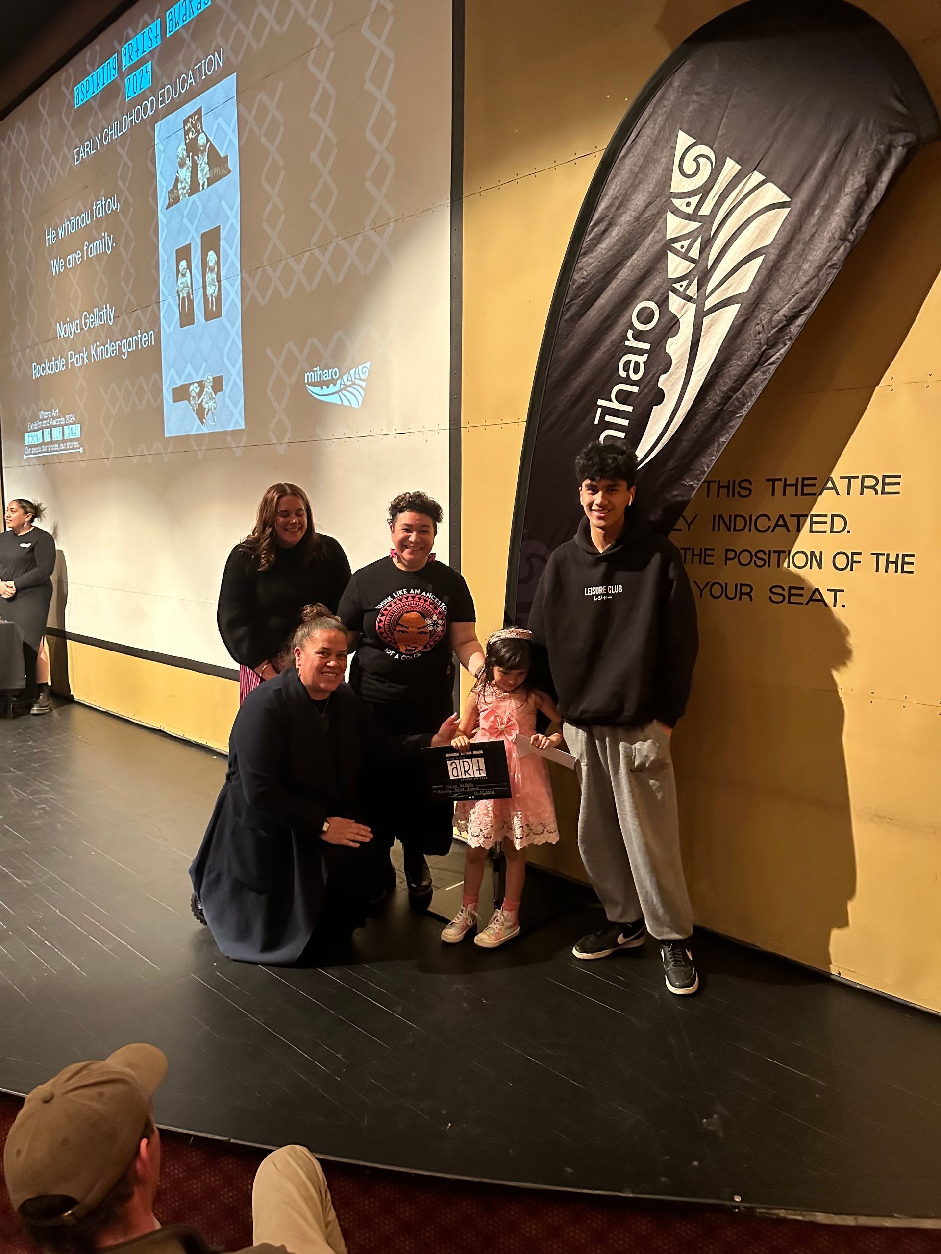 A group of people standing on a stage in front of a large screen.