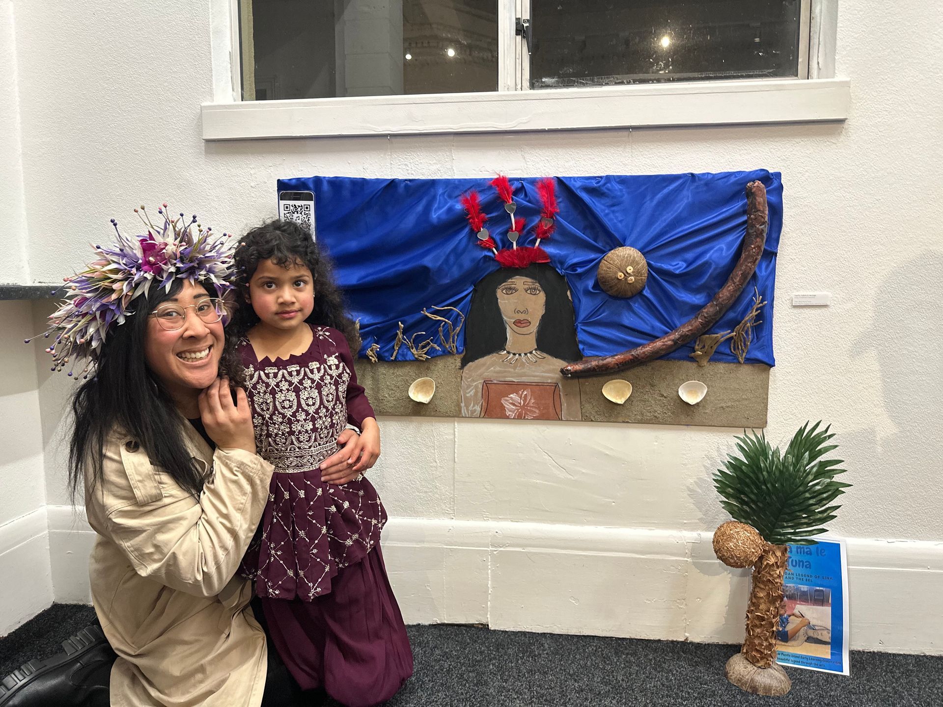 A woman and a little girl are posing for a picture in front of a painting.
