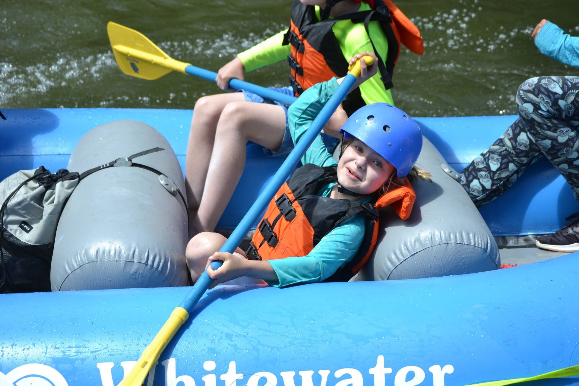 A boy in a blue helmet is holding a paddle in a whitewater raft