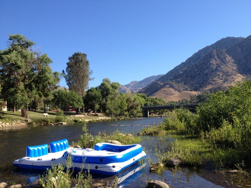 An inflatable blue and white raft sits on the river with a mountain as a backdrop