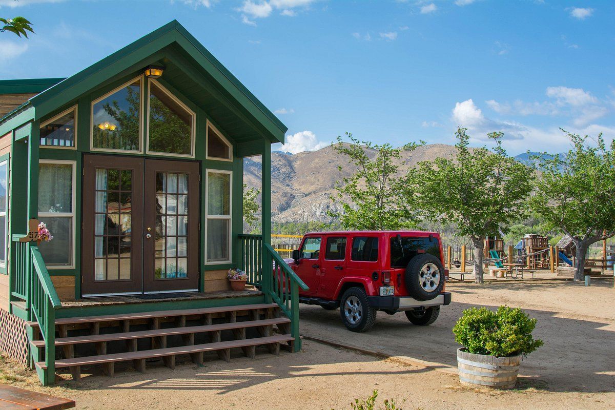 A red jeep is parked outside of a cabin with a playground in the distance