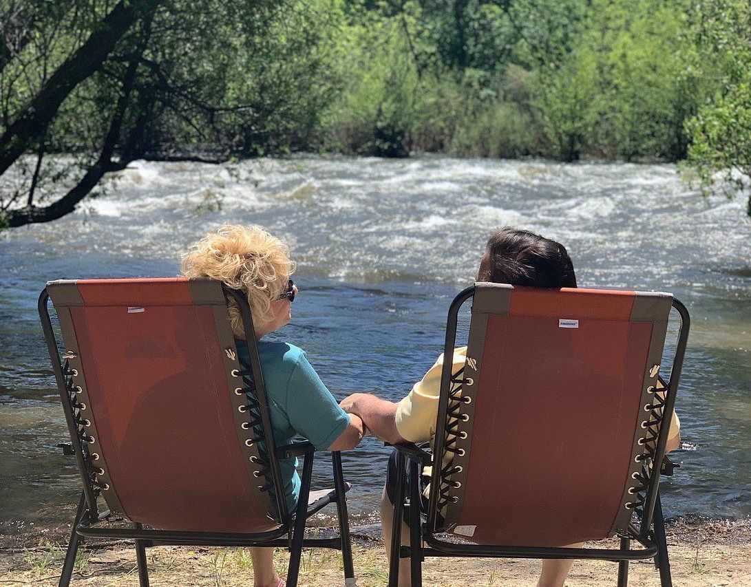 Two people sitting in camp chairs by the river look at each other