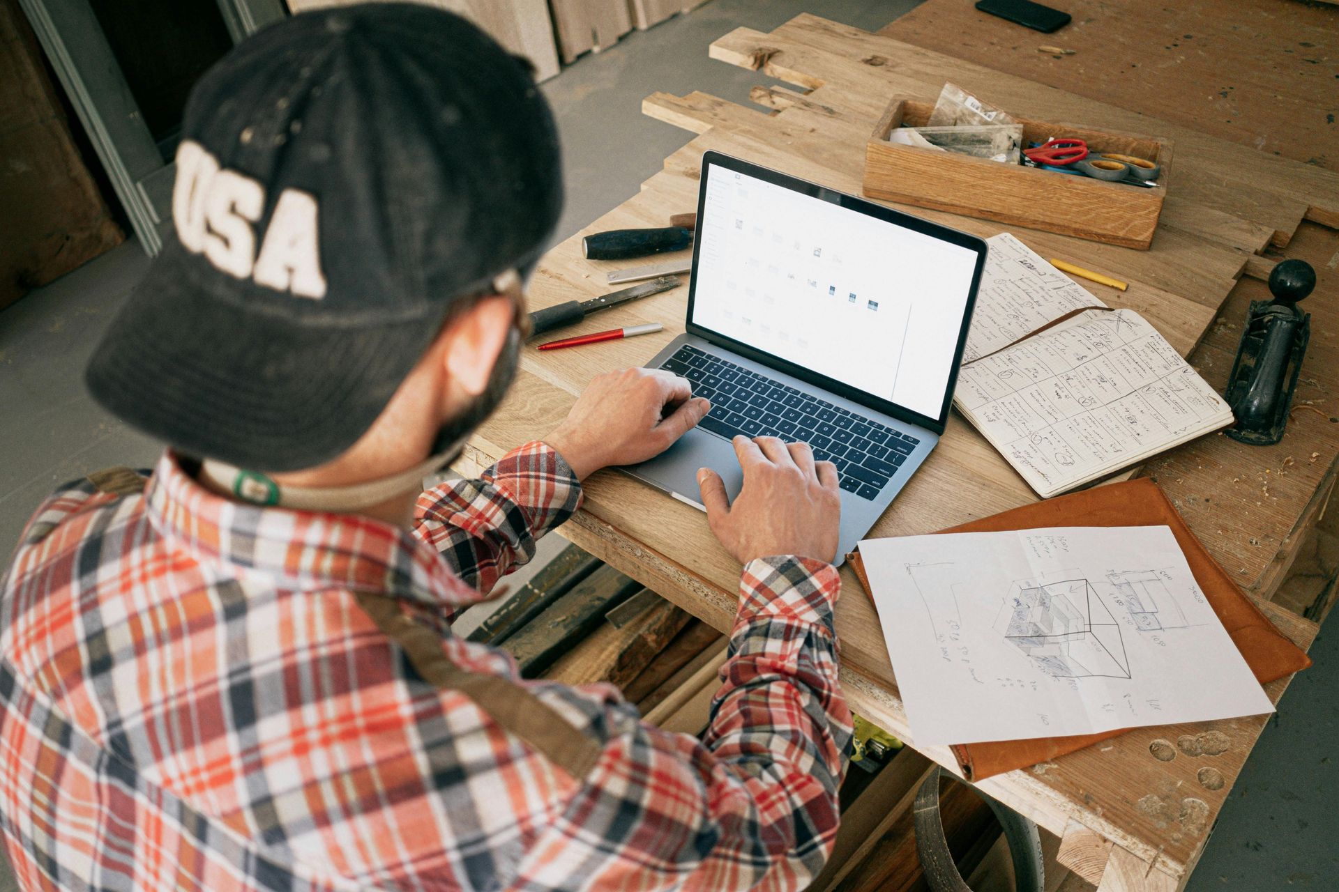 A man sat at a laptop with notebooks making plans.