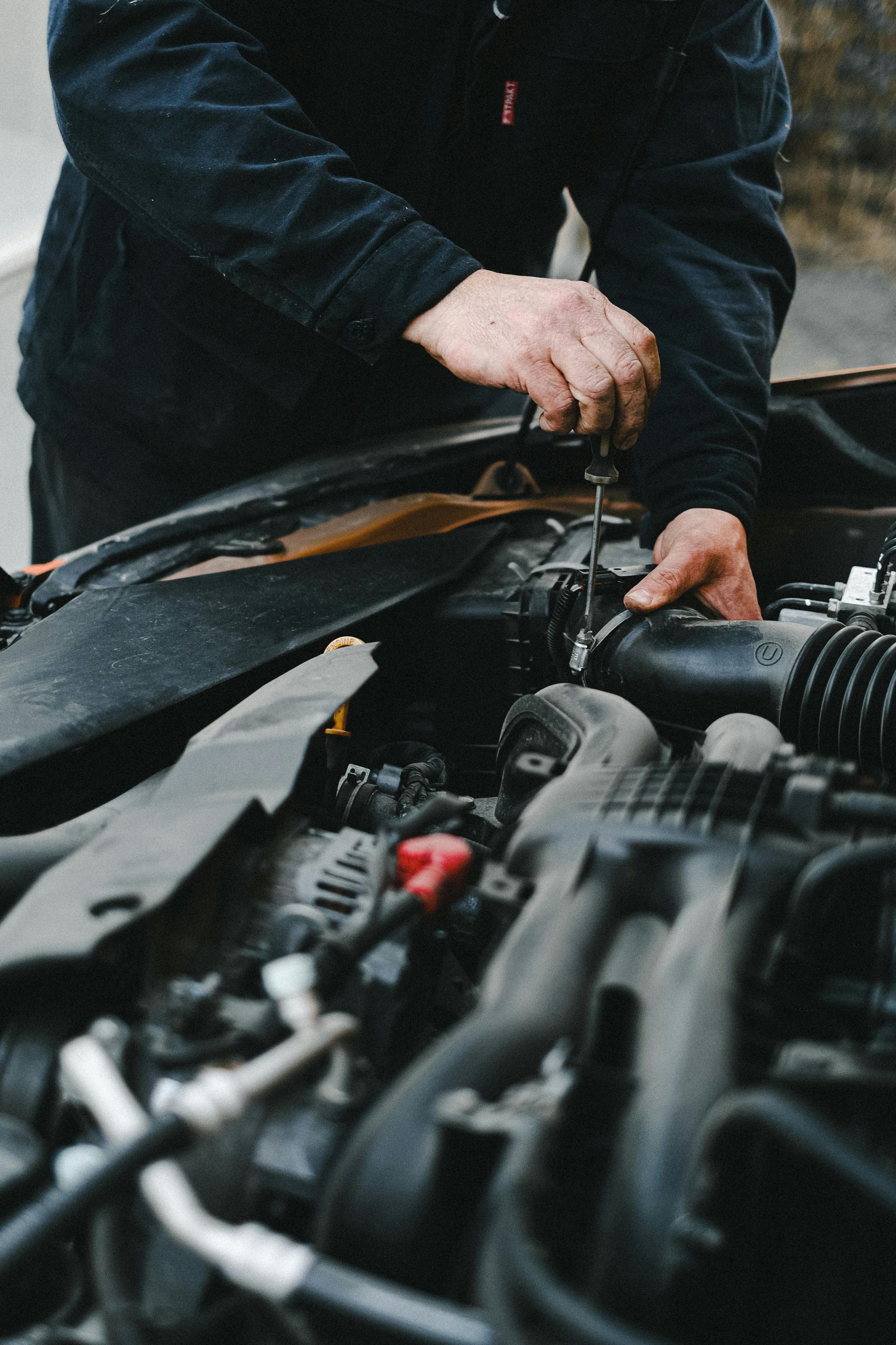 A man is working on a car engine with a screwdriver.