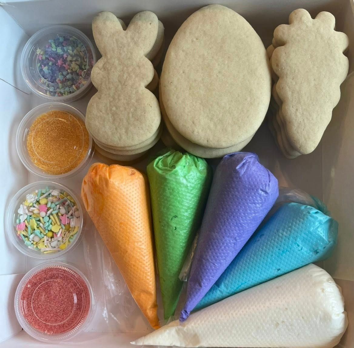 Easter cookie decorating kit: Bunny, egg, carrot-shaped cookies, icing bags, sprinkles, and toppings in a box.