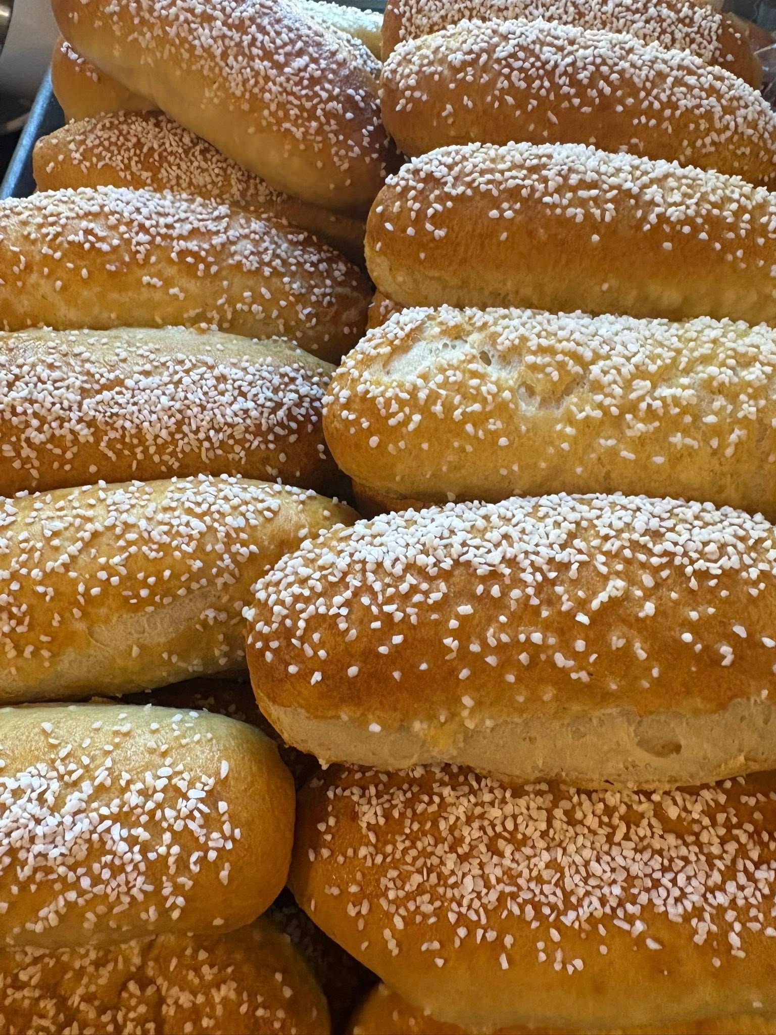Close-up of a pile of golden-brown, oblong-shaped rolls sprinkled with white sugar crystals.