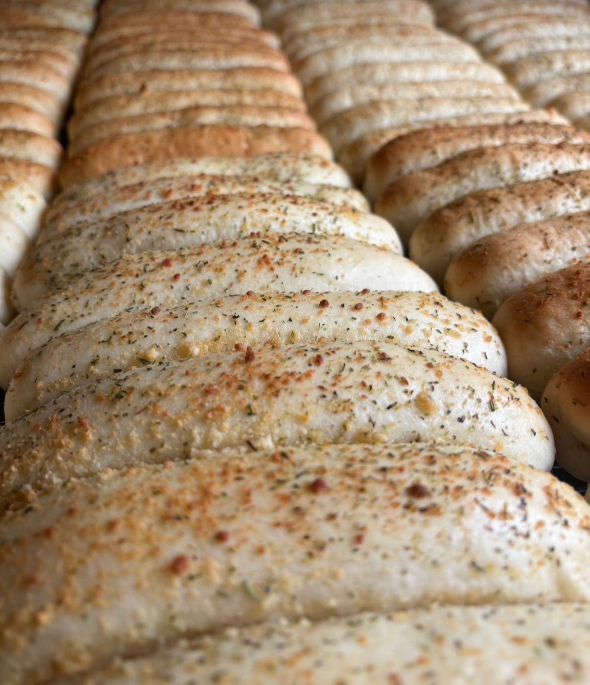 Rows of baked breadsticks, seasoned with herbs and spices.