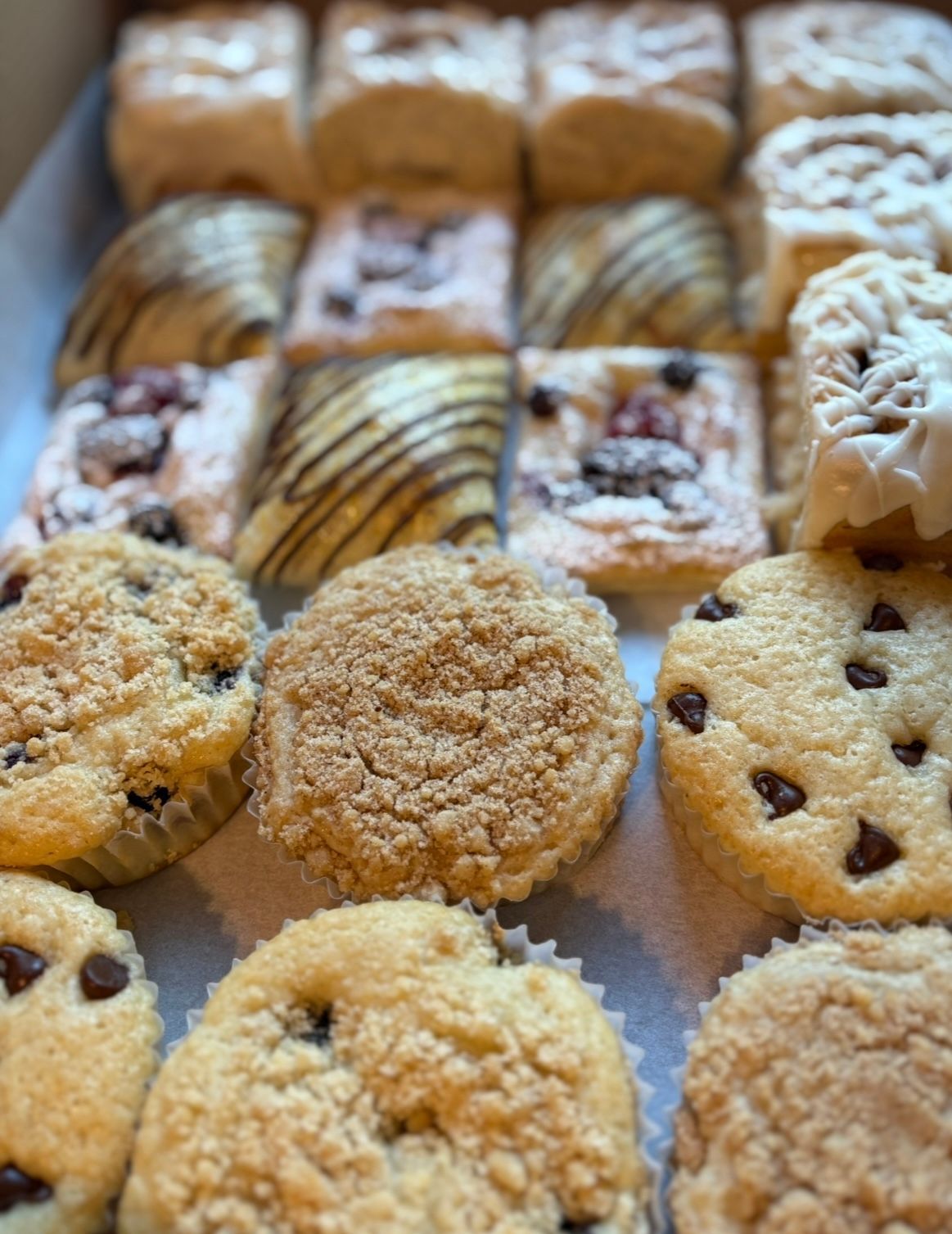 Assortment of baked pastries in a box: muffins, danishes with chocolate chips and crumb topping.