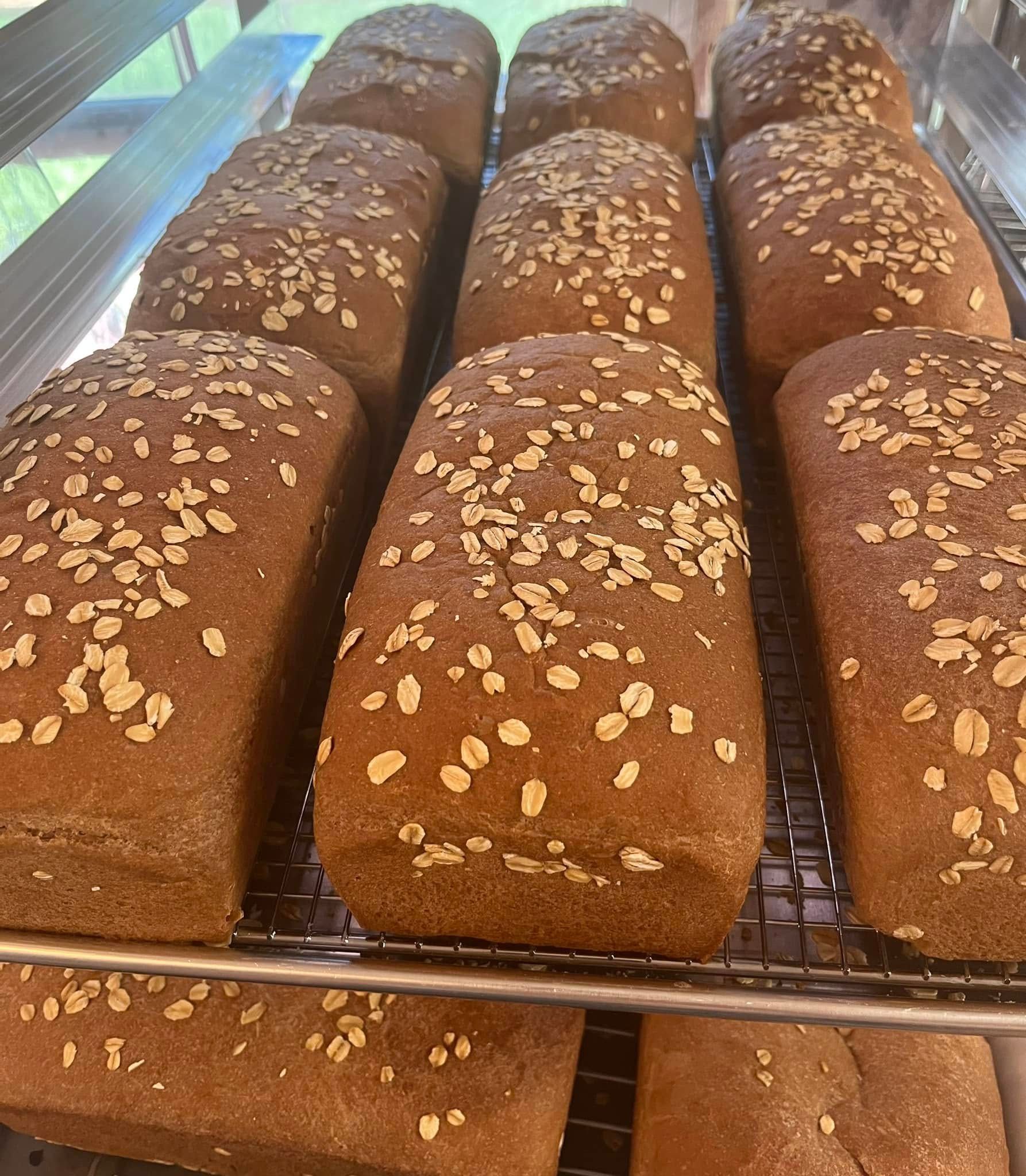 Loaves of brown bread topped with oats, cooling on a wire rack.