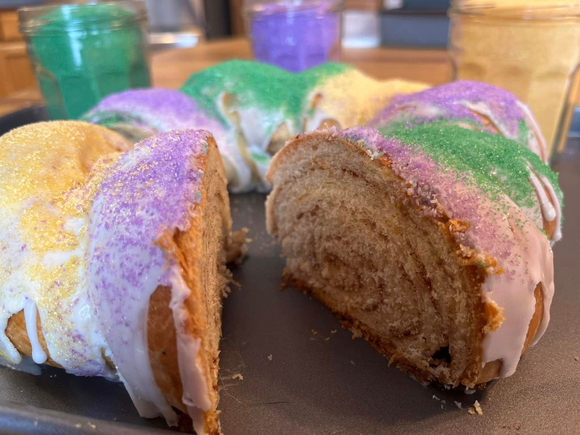King cake with colored sugar sprinkles and a cut section revealing the cinnamon swirl.