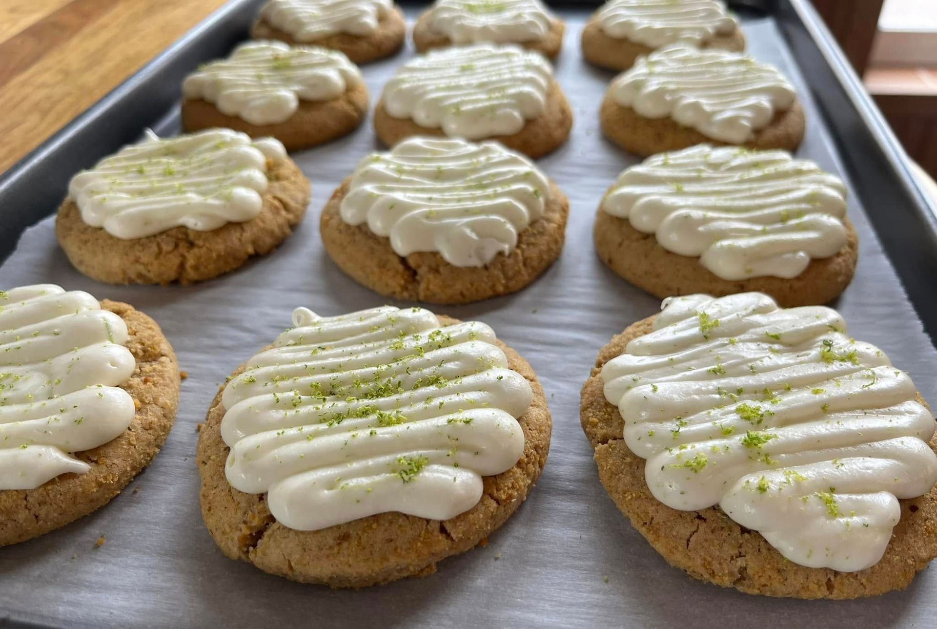 Cookies with white frosting and lime zest on a baking sheet.