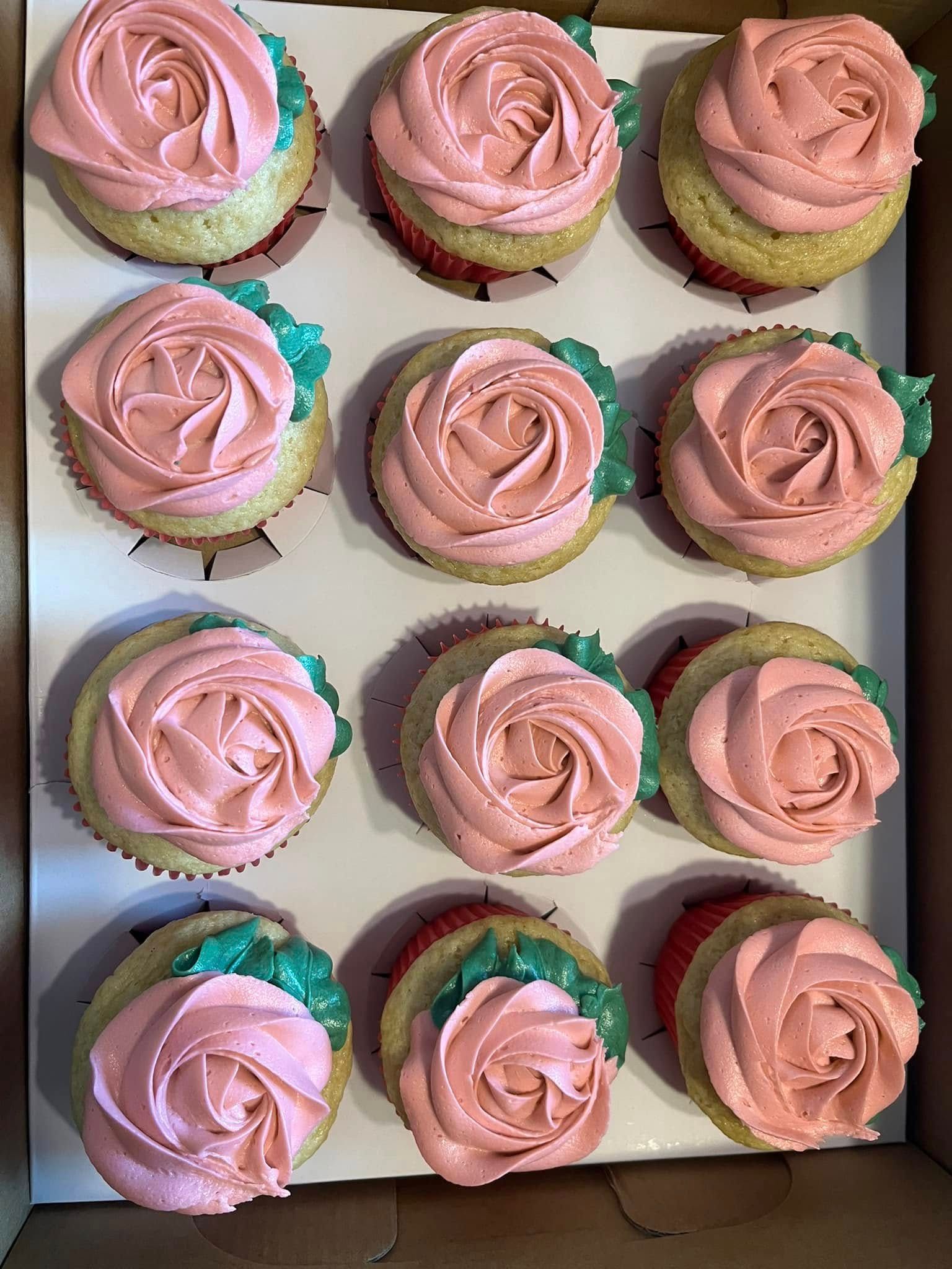 Box of a dozen cupcakes with pink rose frosting and green leaf accents.