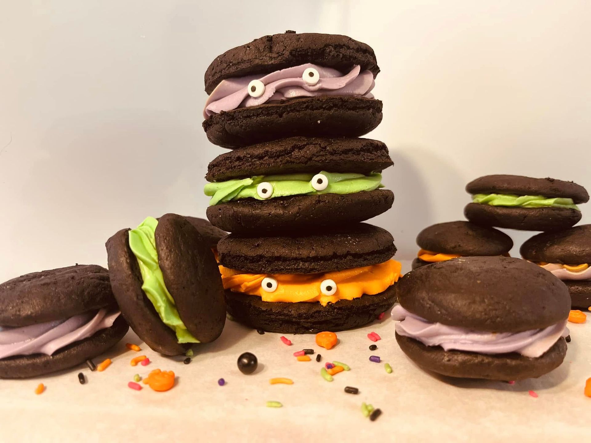 Chocolate sandwich cookies stacked and scattered with colorful frosting faces, Halloween theme.