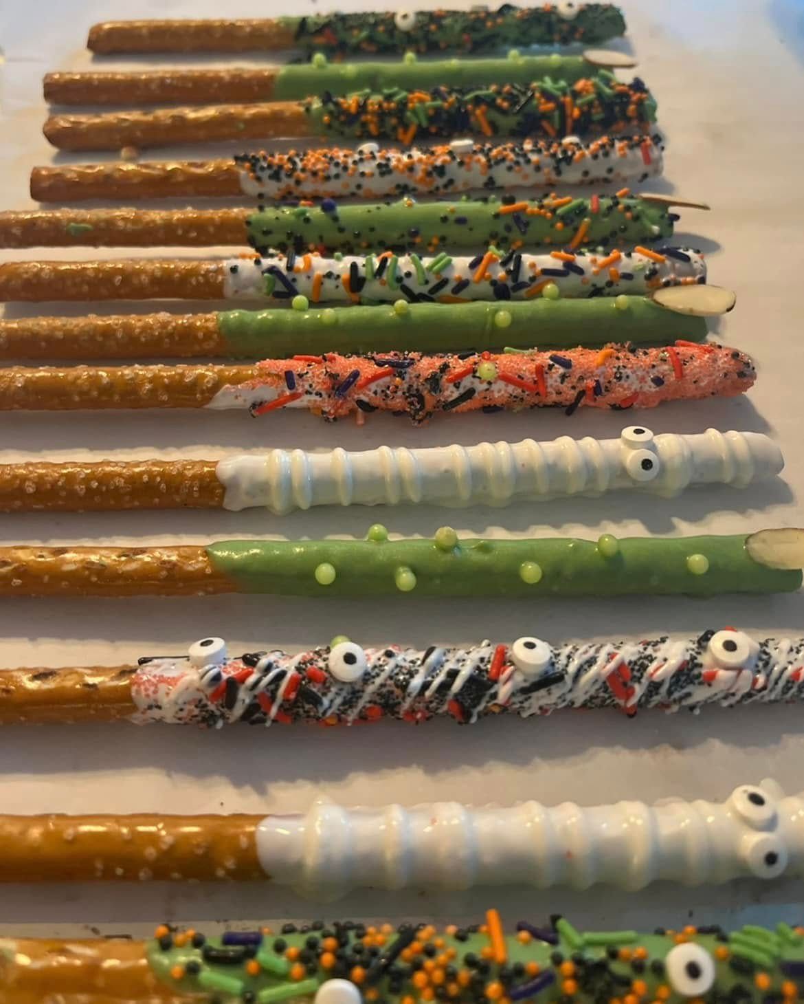 Halloween-decorated pretzel rods. Several rods dipped in white, orange, and green chocolate, with sprinkles and candy eyes.