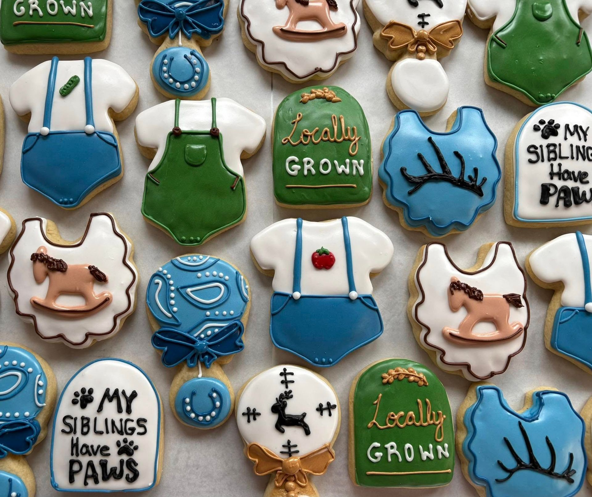 Decorated sugar cookies with farm animal and baby clothes designs in various colors.