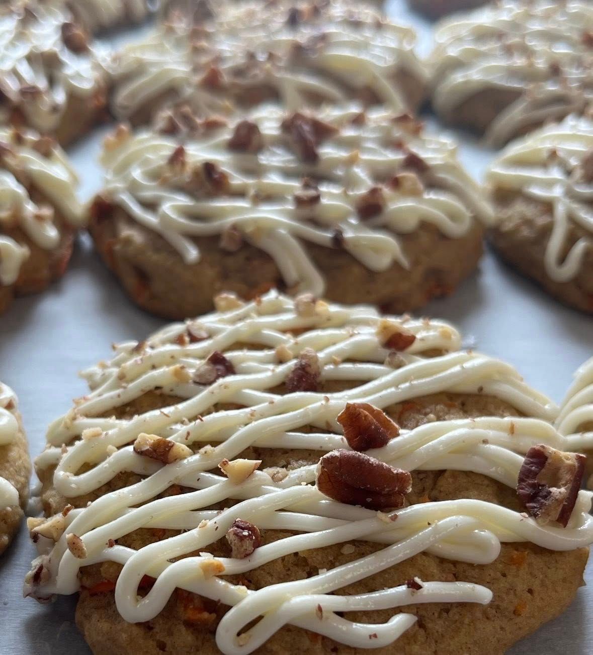 Frosted carrot cake cookies with chopped nuts, arranged on parchment paper.