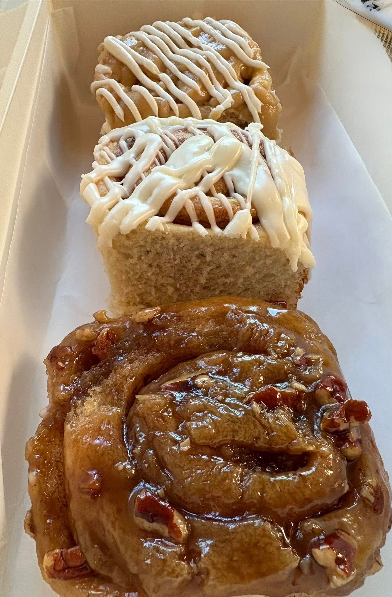 Three cinnamon rolls, one pecan, drizzled with icing, stacked in a white container.
