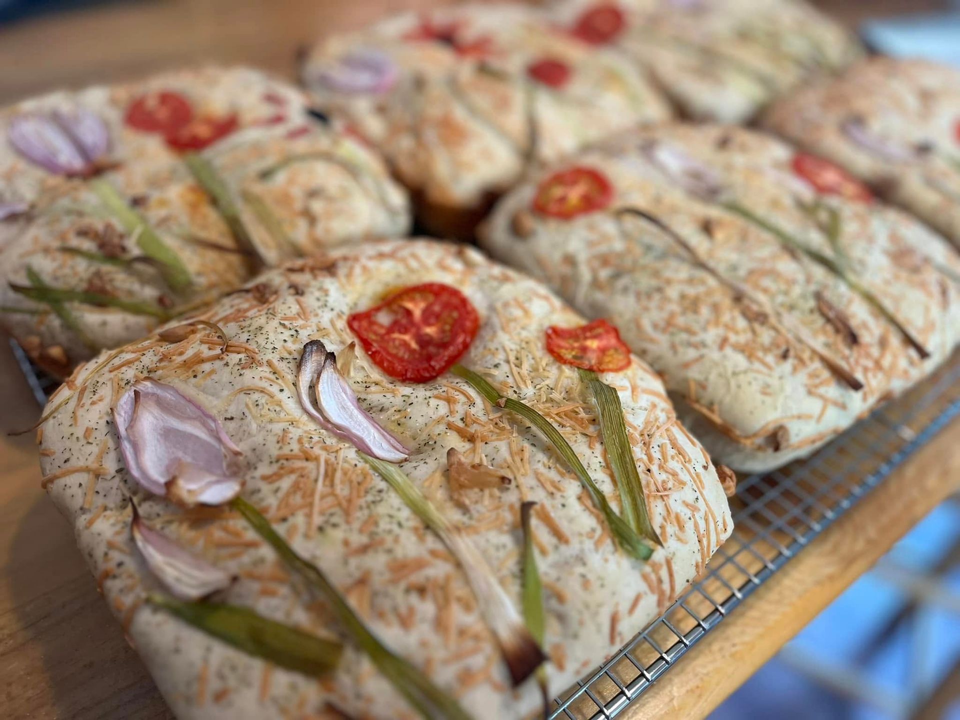 Focaccia bread decorated with tomatoes, onions, and chives, baked on a wire rack.