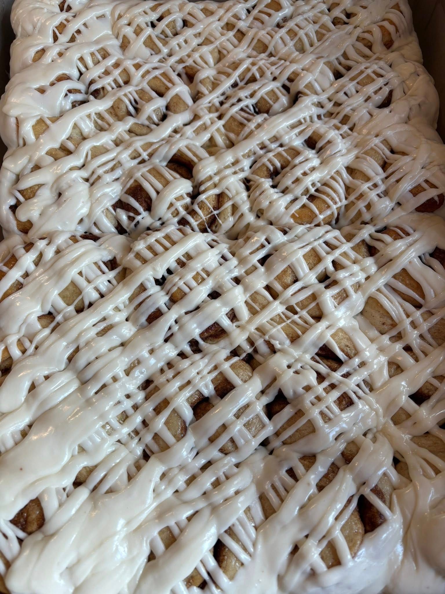 Overhead view of frosted cinnamon rolls in a baking pan, drizzled with white icing.