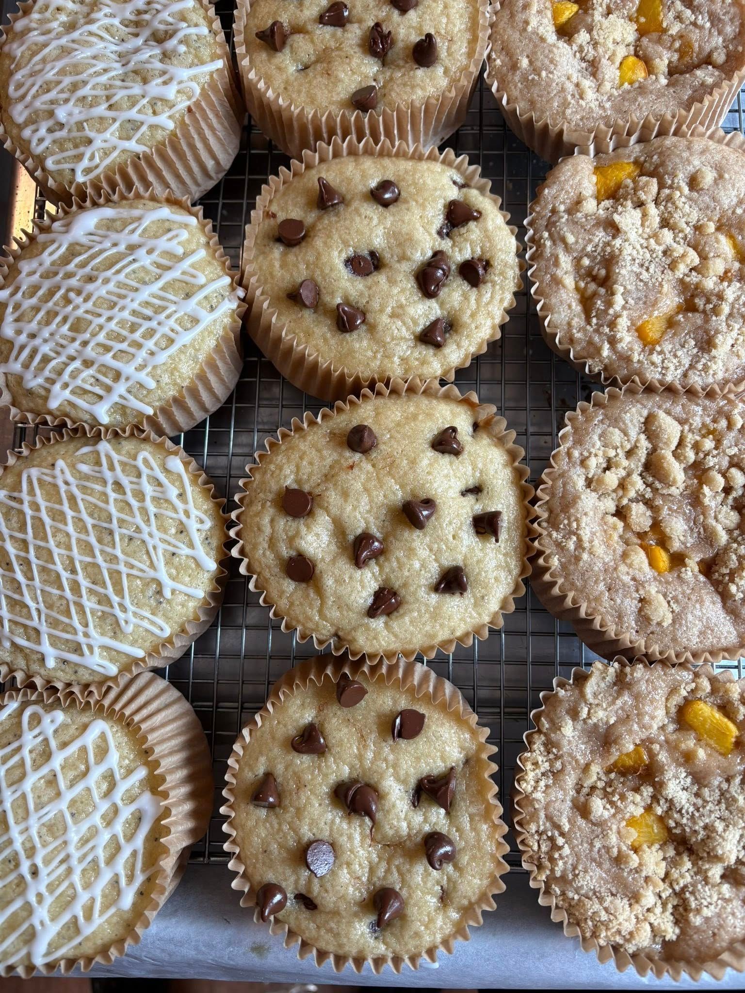 Top-down view of a dozen muffins: glazed, chocolate chip, and fruit-topped, arranged on a cooling rack.