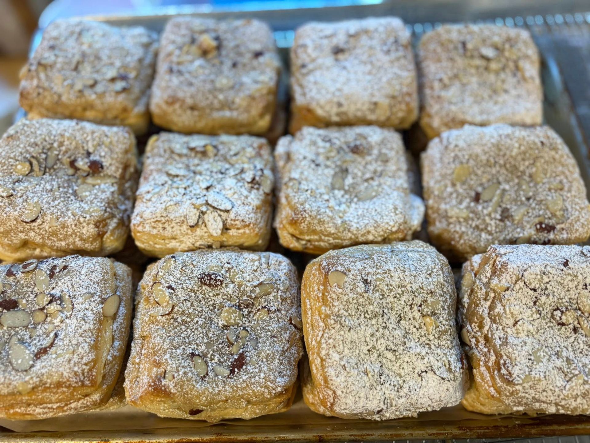 Close-up of a tray with a dozen square pastries, topped with almonds and powdered sugar.