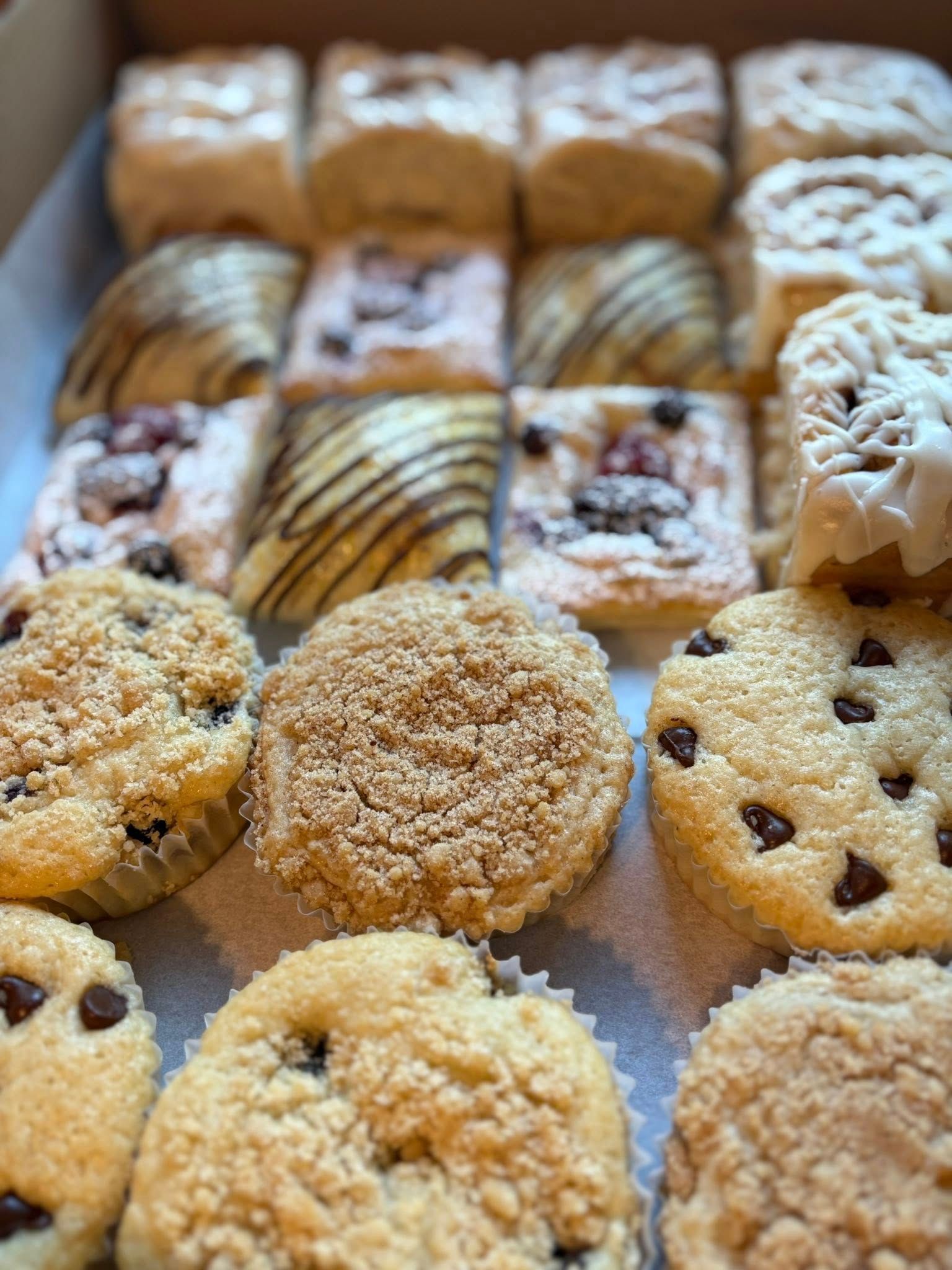 Box of various pastries: muffins, scones, and danishes with chocolate chips and frosting.