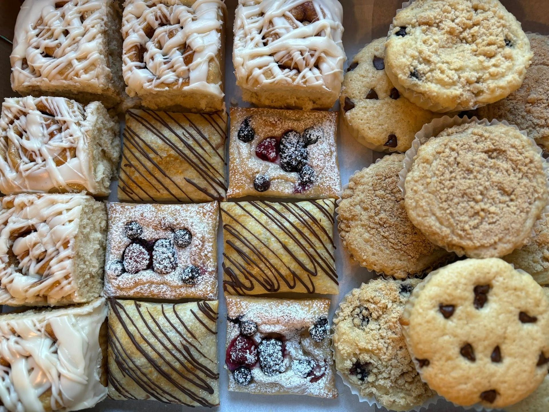 Assortment of pastries: iced squares, berry-topped squares, and chocolate chip cookies in a box.