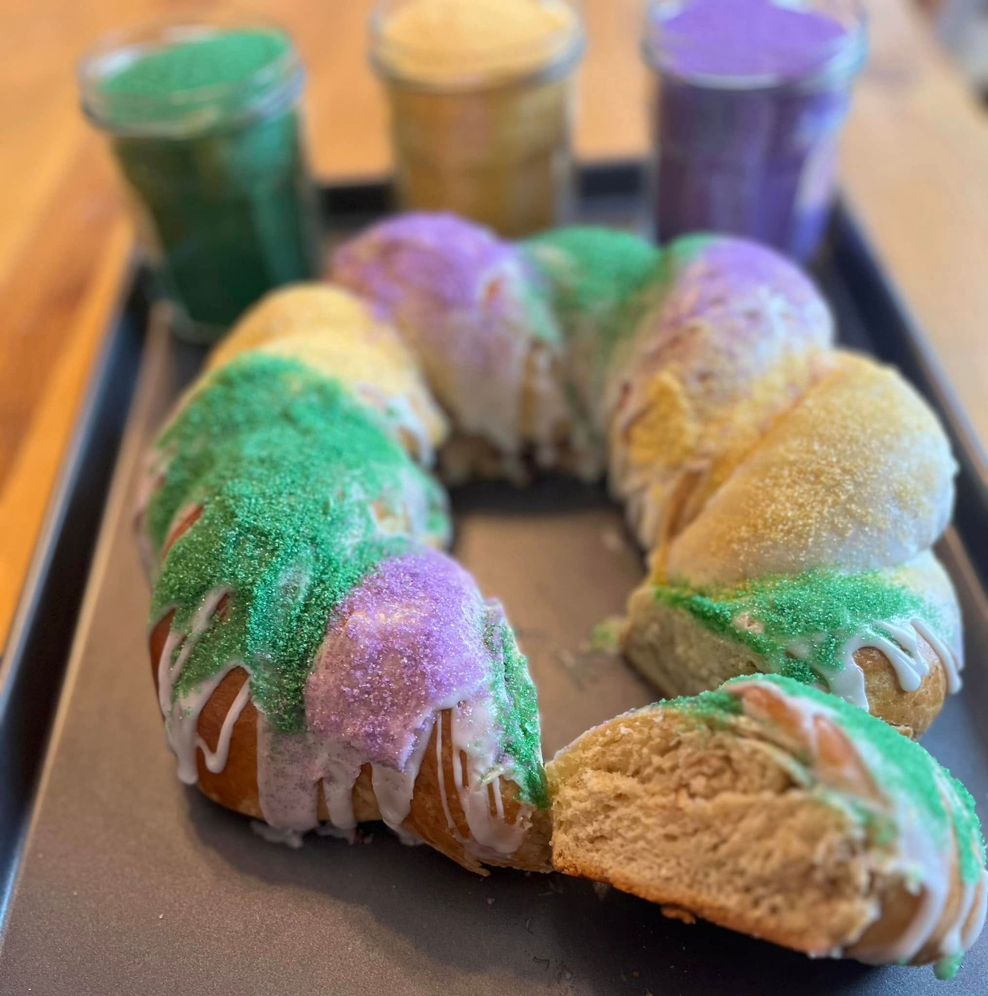 King cake with purple, green, and yellow sugar, served with colored sugar jars on a tray.