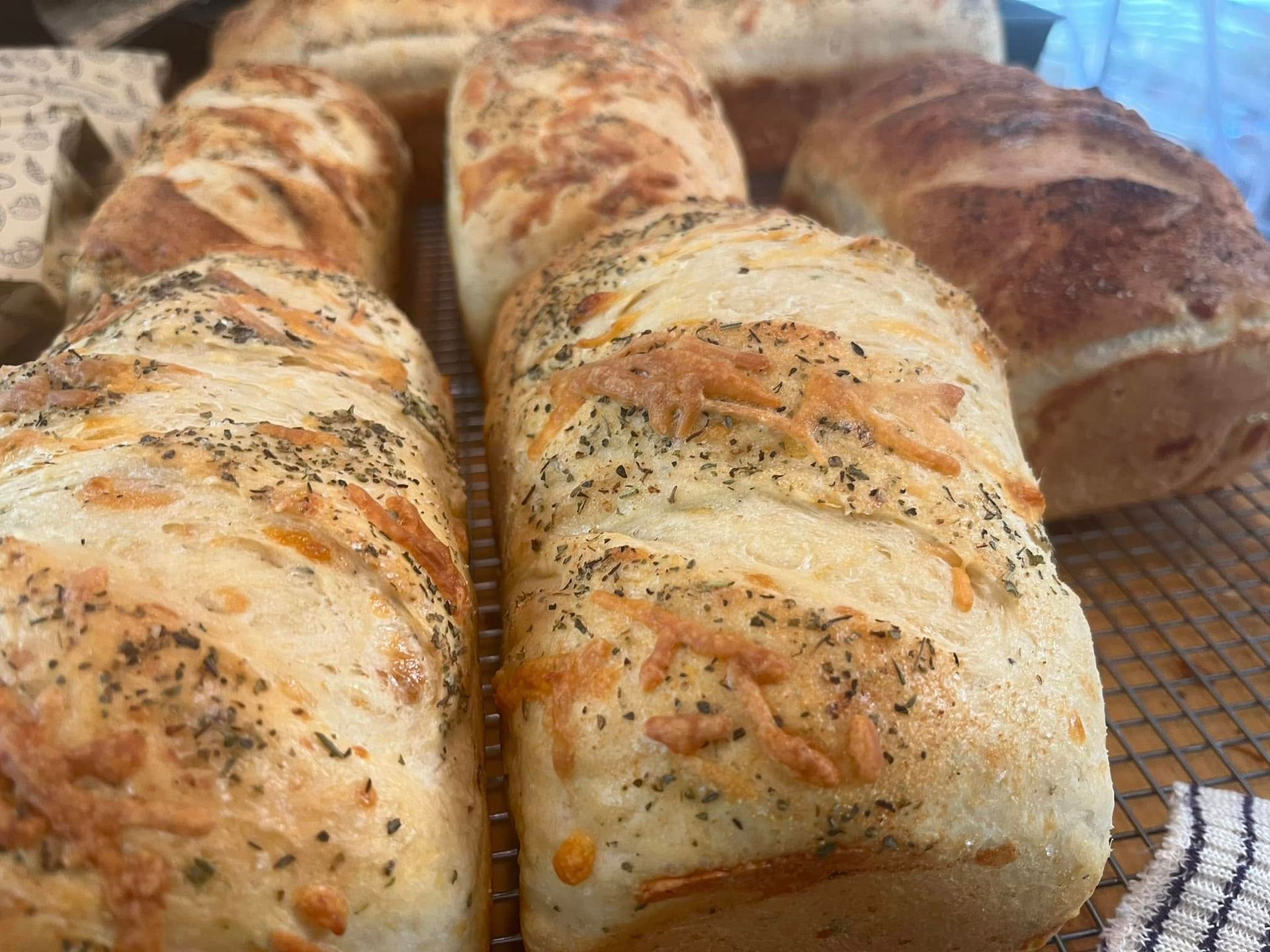 Loaves of bread topped with herbs and cheese on a wire rack.