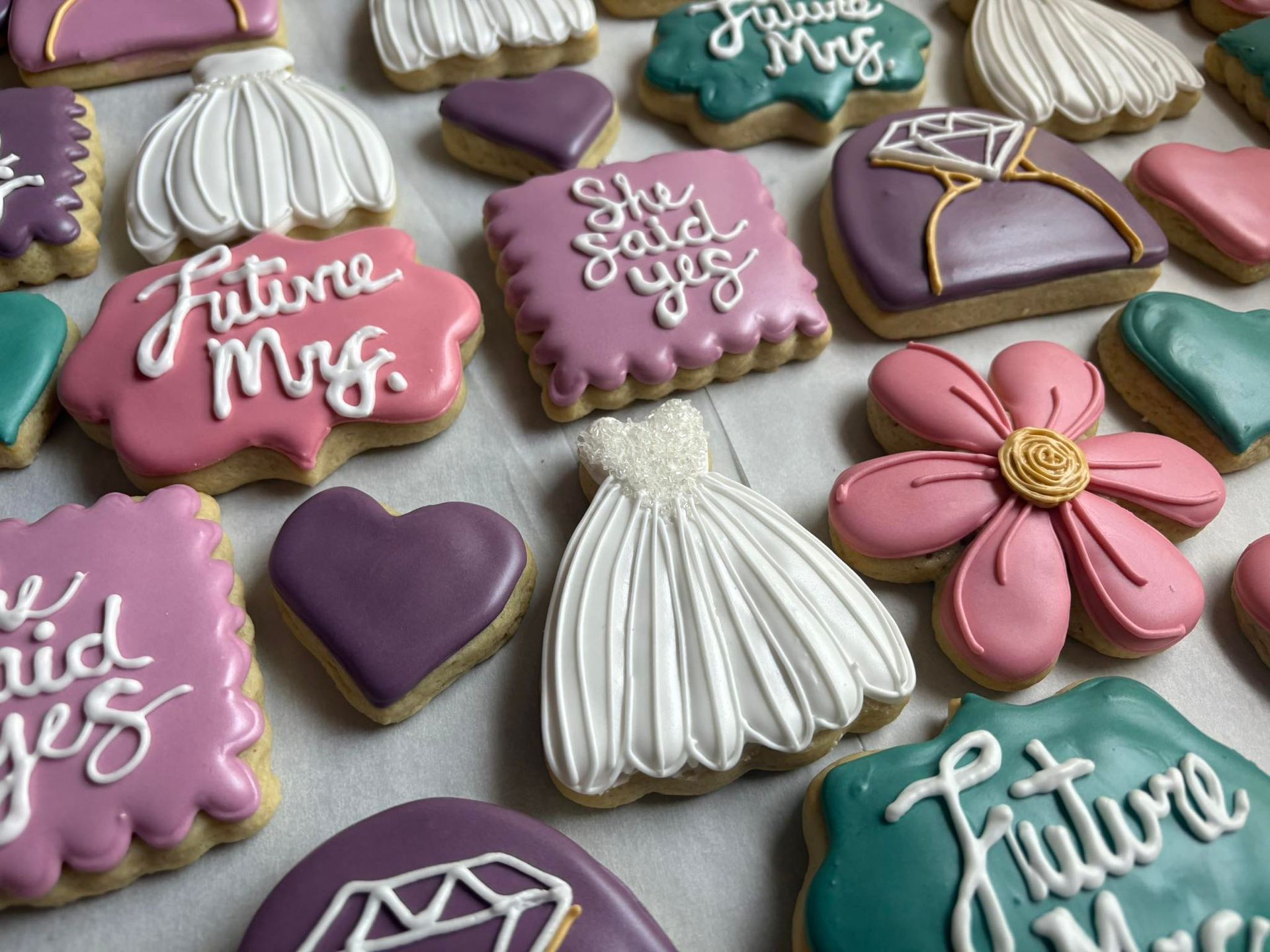 Decorated sugar cookies: wedding-themed shapes in pink, teal, white, and purple with icing details.