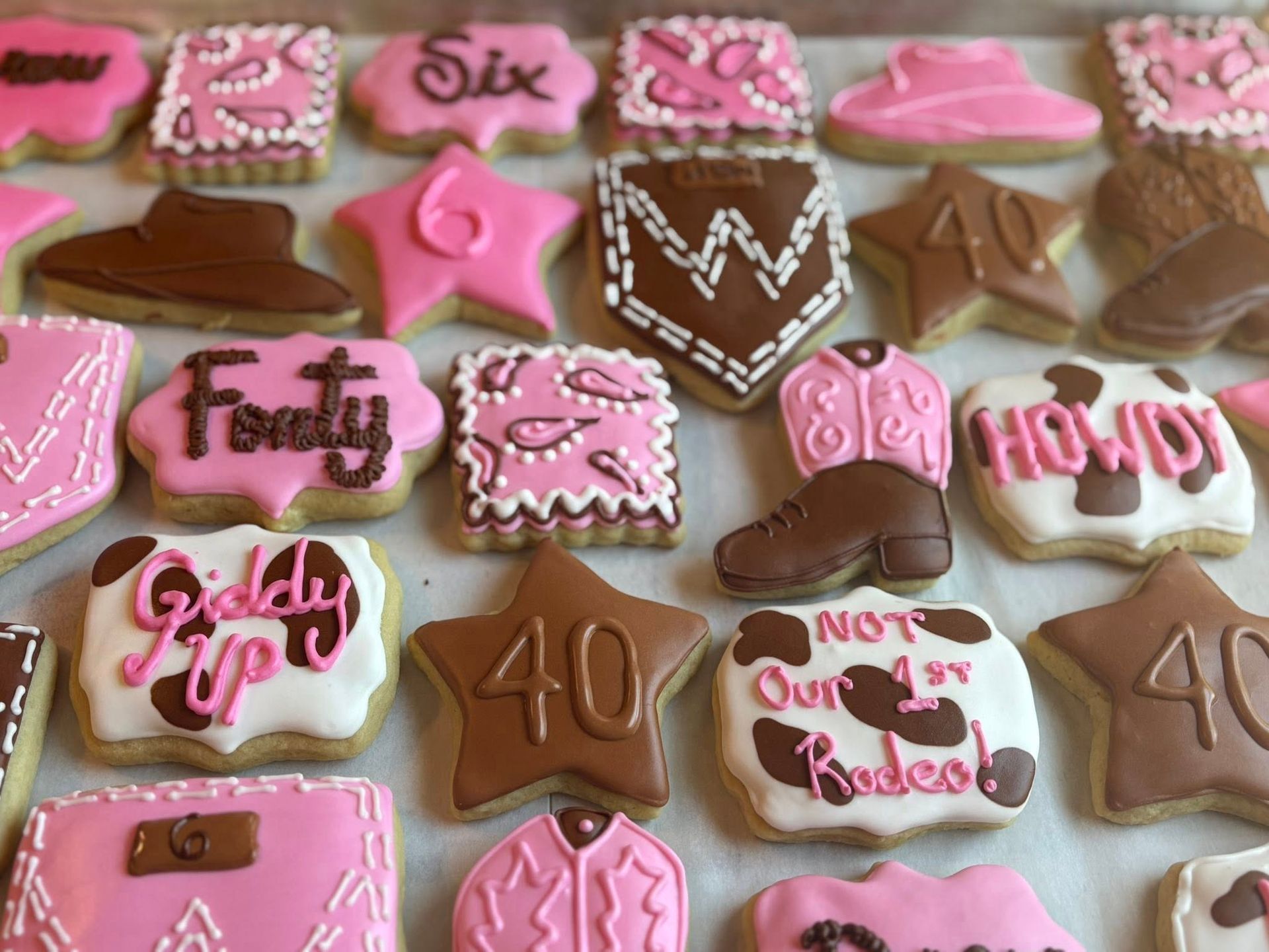Assortment of decorated sugar cookies in pink and brown with western and birthday themes.