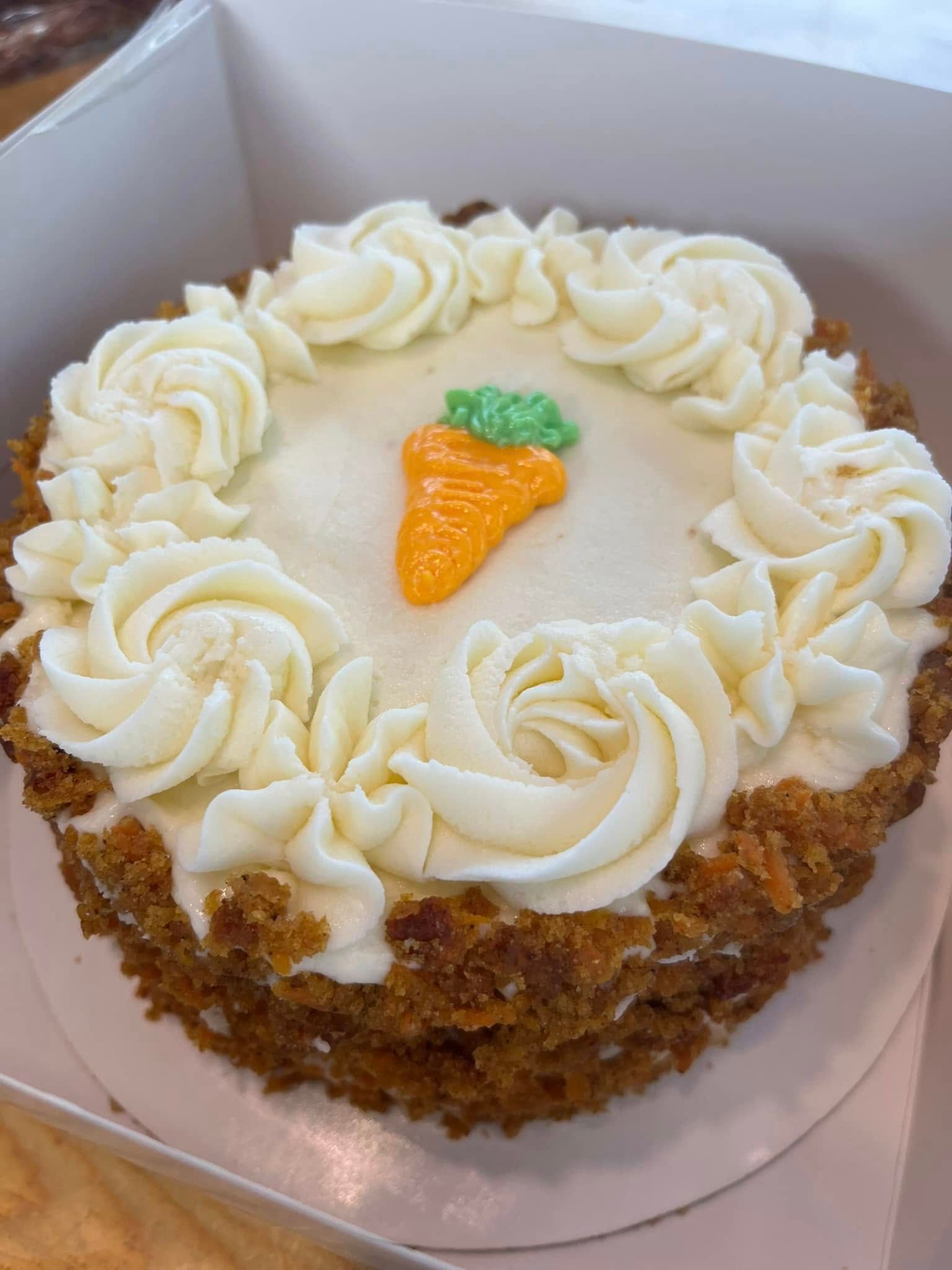 Carrot cake with white frosting swirls and a candy carrot on top.